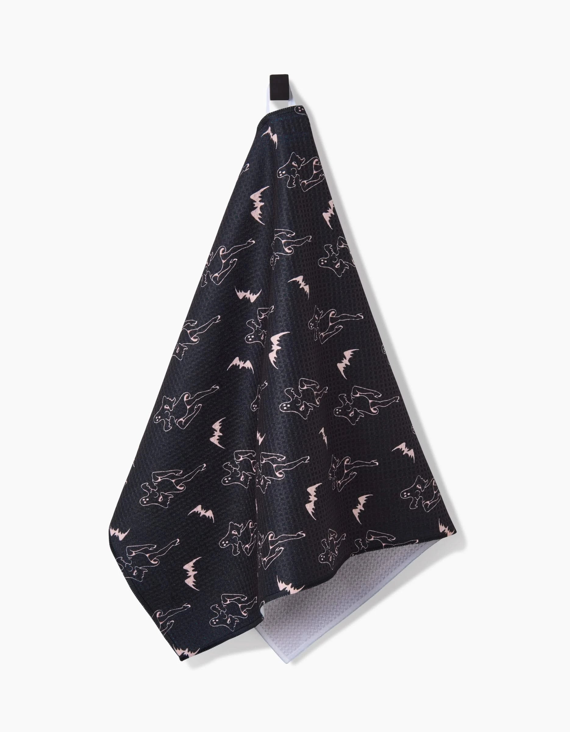 The Ghost Pin Up tea towel by Cole Strem features white and pink dinosaur and lightning bolt outlines on a dark Geoweave fabric, hangs from a black loop, has a textured surface, white backing, and is made with recycled materials.