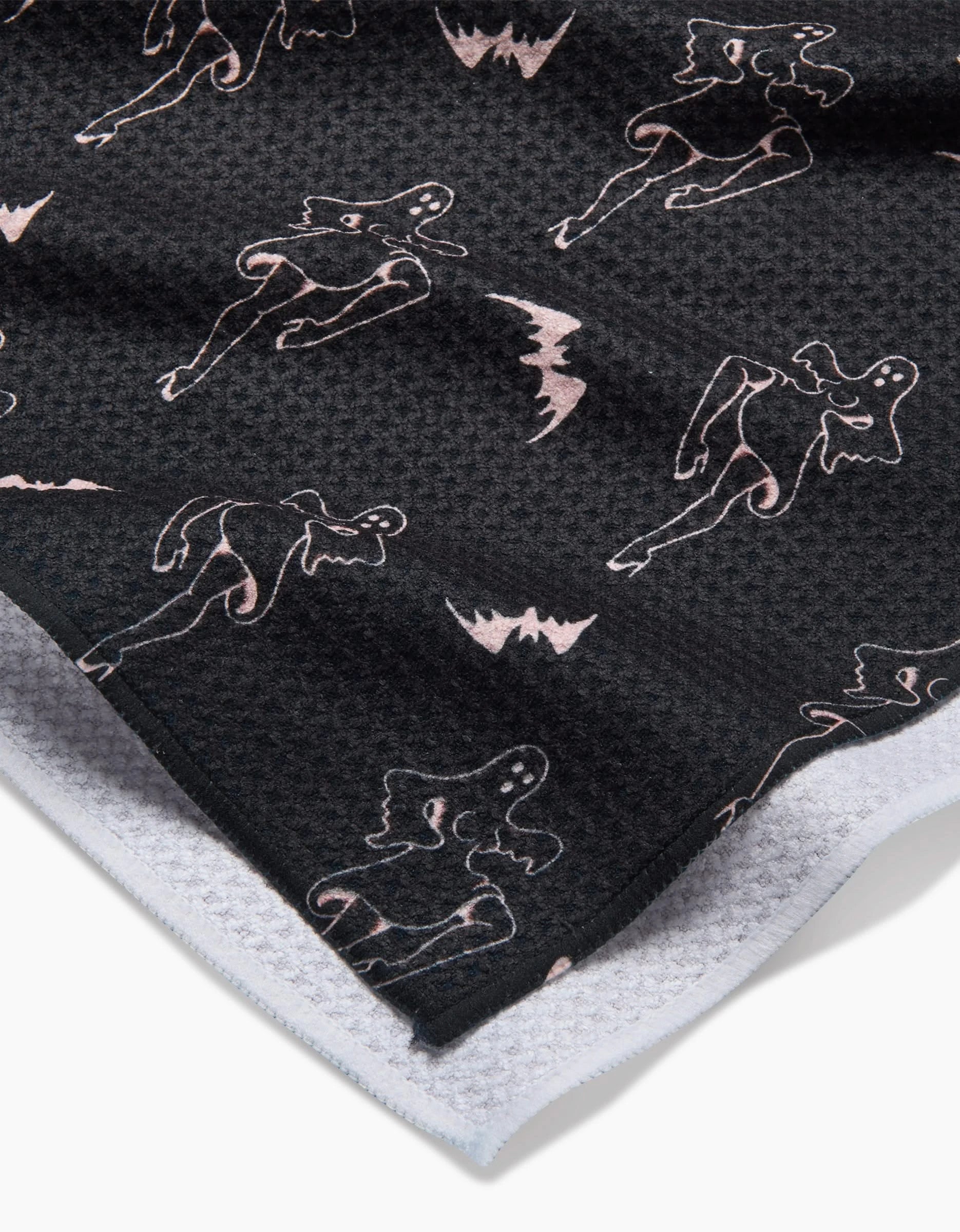 A close-up of the Cole Strem Ghost Pin Up tea towel. It features black Geoweave fabric with light pink outlined abstract figures and bats, a textured surface, white terry cloth reverse, and is made from recycled materials.