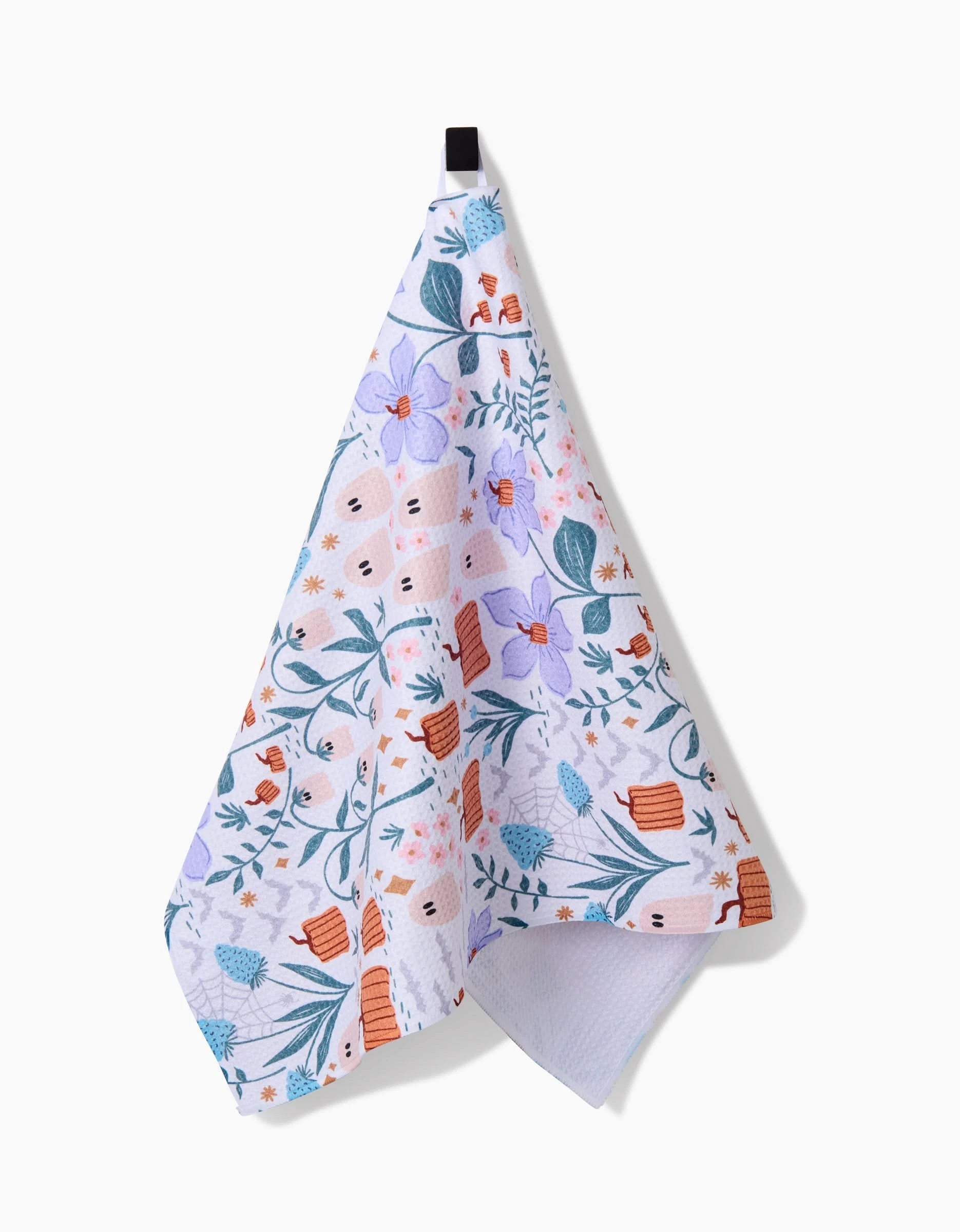 The Ghosts In The Garden tea towel by Charlie Rowan Designs features a quick-drying white fabric with vibrant blue, purple, orange, and pink floral patterns. It hangs from a black loop against a plain white background.