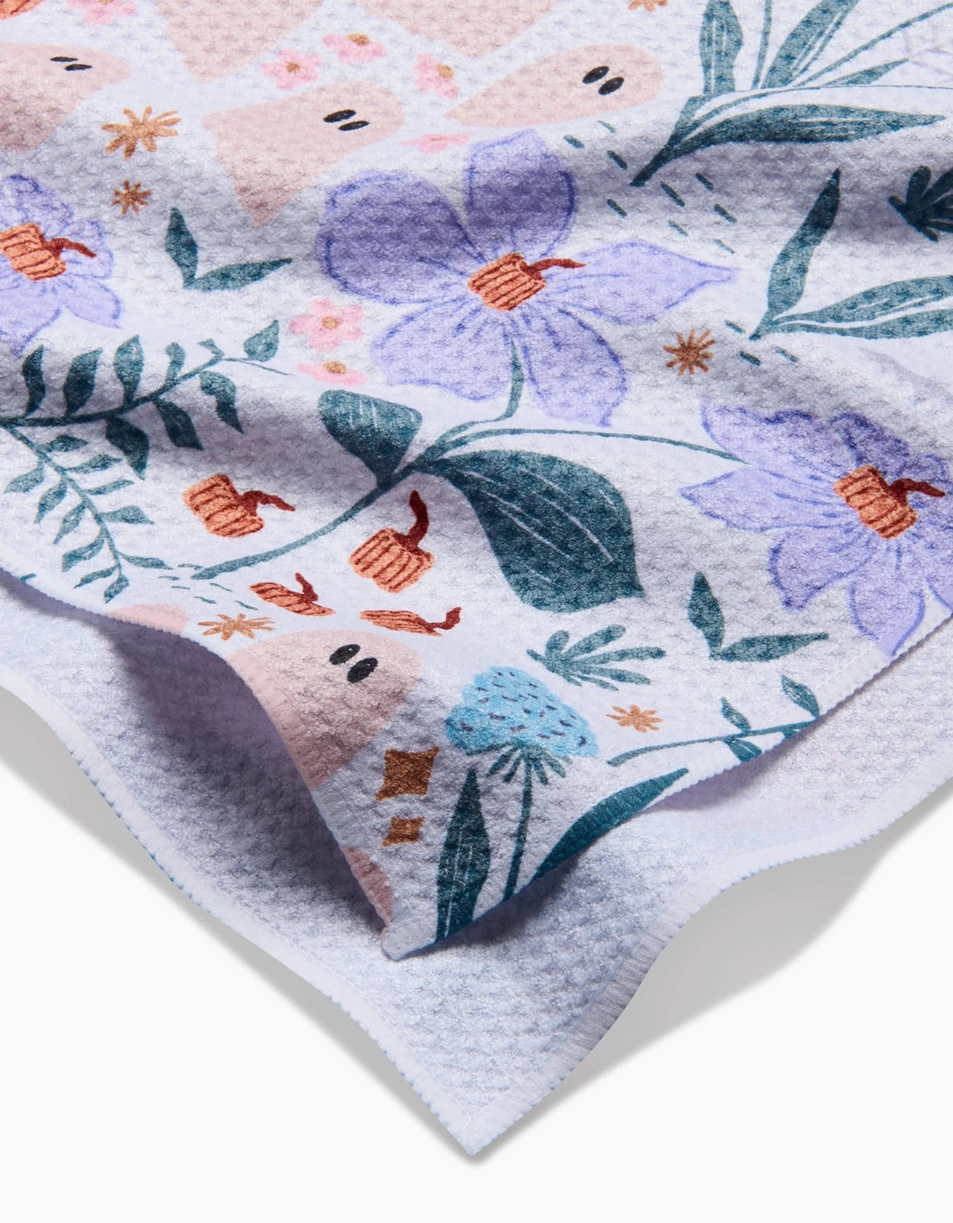 A close-up of the Ghosts In The Garden tea towel by Charlie Rowan Designs, featuring a colorful floral pattern on a light background—crafted from quick-drying recycled materials.