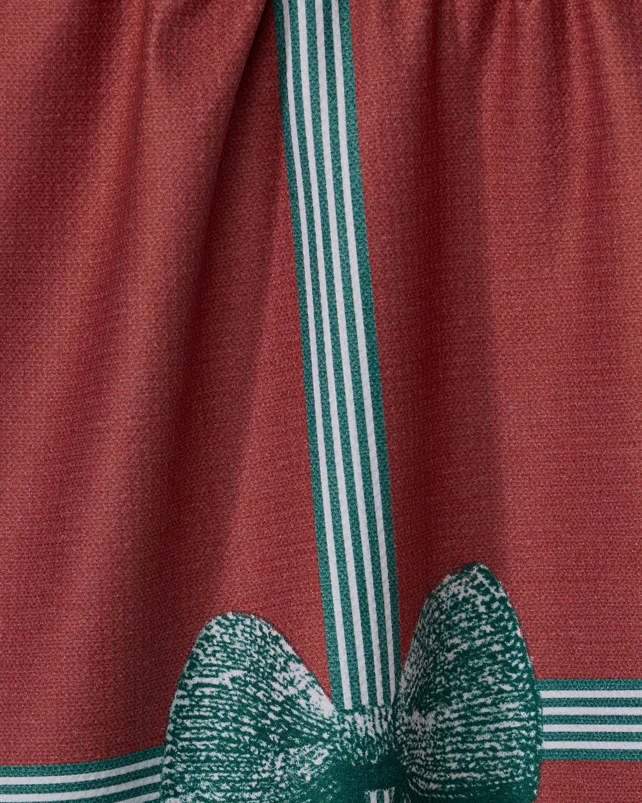 Close-up of Geometry’s “Gifted” tea towel: features a reddish-brown color with green and white vertical stripes, a green bow print at the bottom, and visible texture, stitching, and quality of its recycled materials.