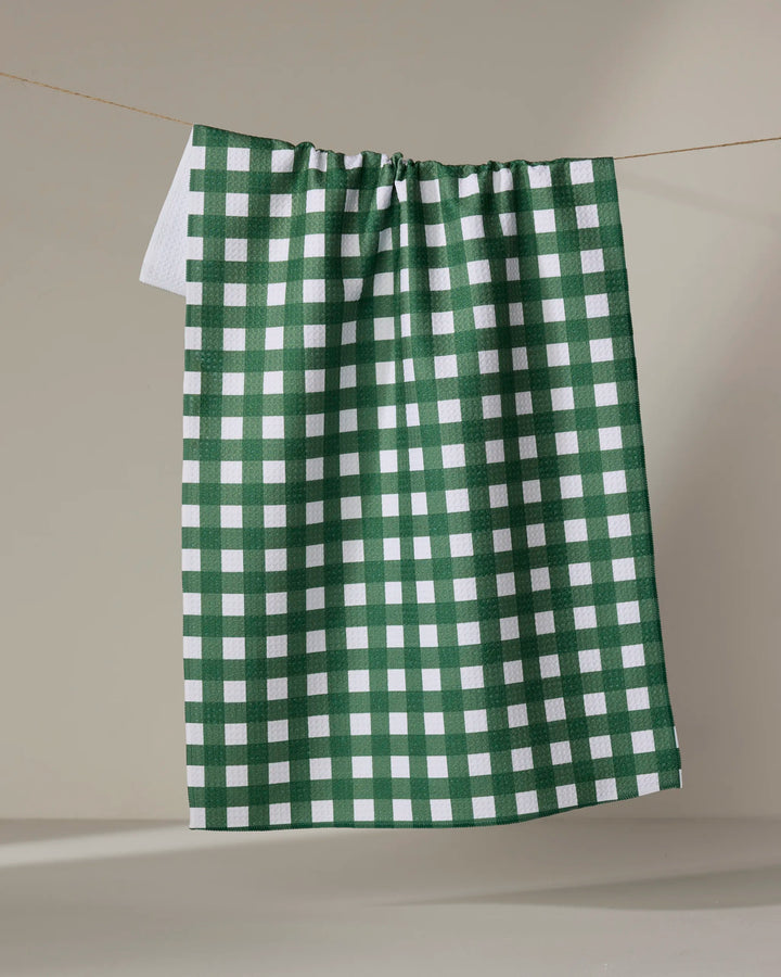 The Buy Guide’s Gigi - Evergreen, an ultra-absorbent green and white checkered tea towel, hangs from a clothesline against a neutral beige background.