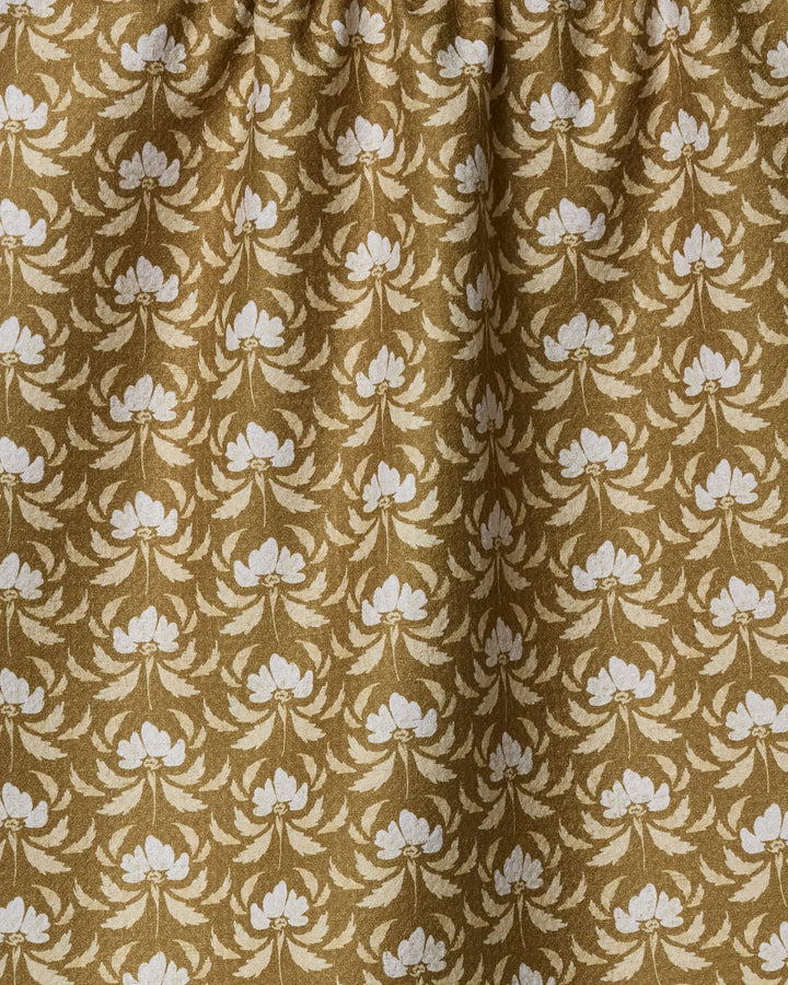 The Gilded Bloom towel by Melissa Johnson features gold and beige fabric with a symmetrical floral pattern of cream flowers and leaves. This quick-drying towel is softly gathered at the top for added elegance.