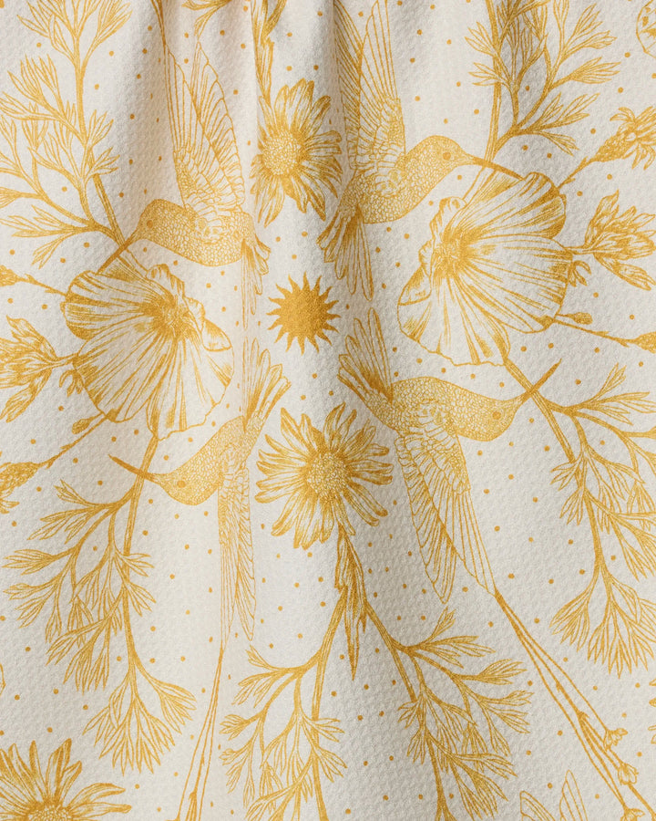 The Gilded Nectar tea towel by Geometry features elegant golden birds, flowers, and leaves in a symmetrical design on white polka-dotted fabric for a stylish, ultra-absorbent, nature-inspired touch.