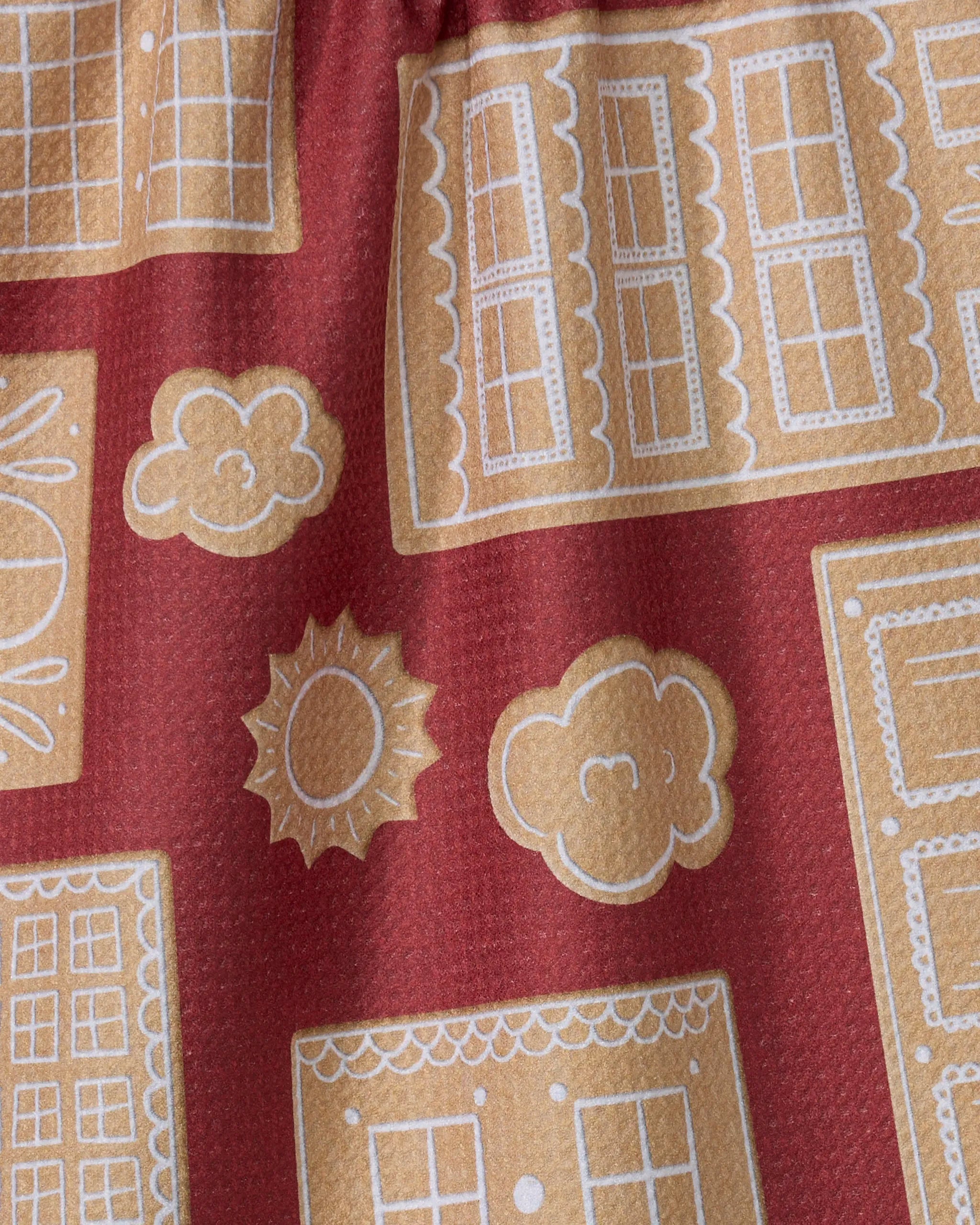A close-up of the Geometry Gingerbread City tea towel, featuring beige window, sun, and cloud designs on a reddish background. Made from recycled materials, its decorative look and eco-friendly appeal add charm to any kitchen.