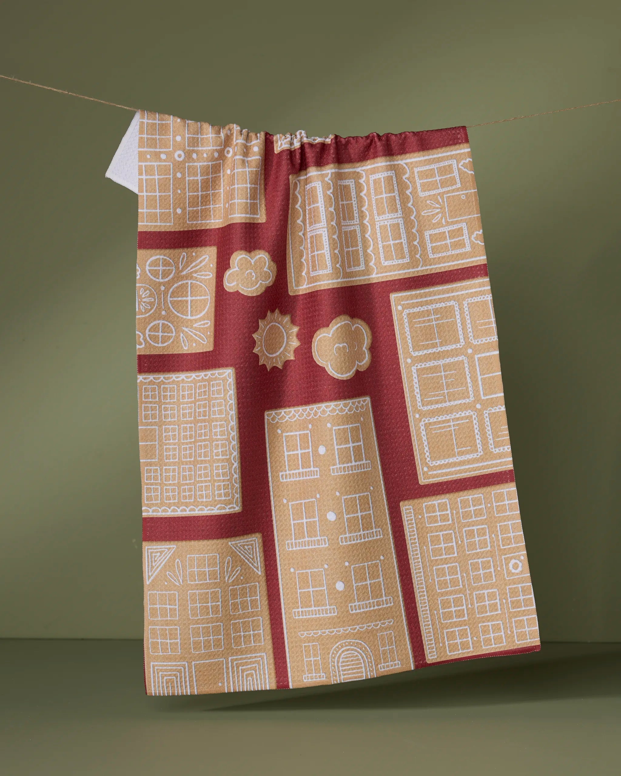 Add charm to your home with Geometry's Gingerbread City hanging fabric kitchen towel, featuring a red and beige pattern with white houses on a muted olive green background—made from recycled materials.