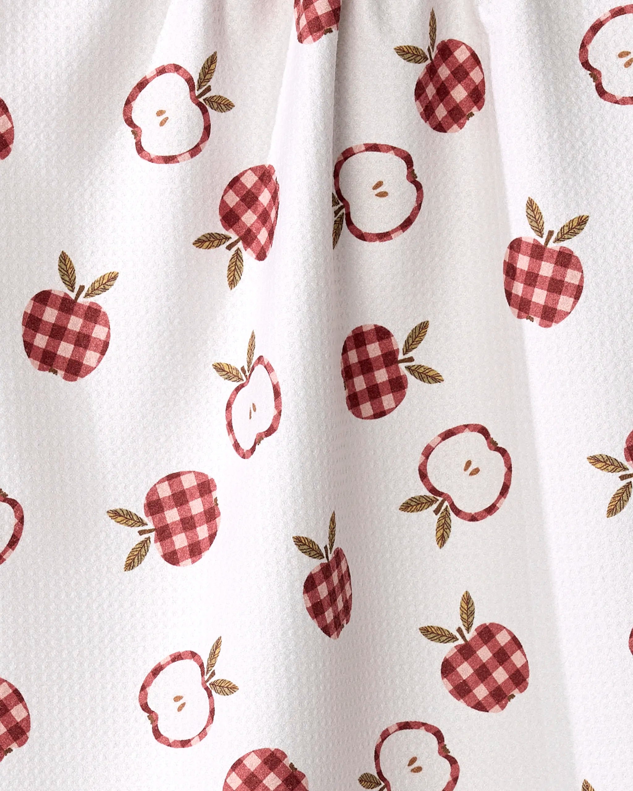 The Gingham Apples tea towel by Teri the Butter features red apples and checkered apple slices with green leaves on textured white fabric. This absorbent towel adds a fresh, cheerful touch to your kitchen.