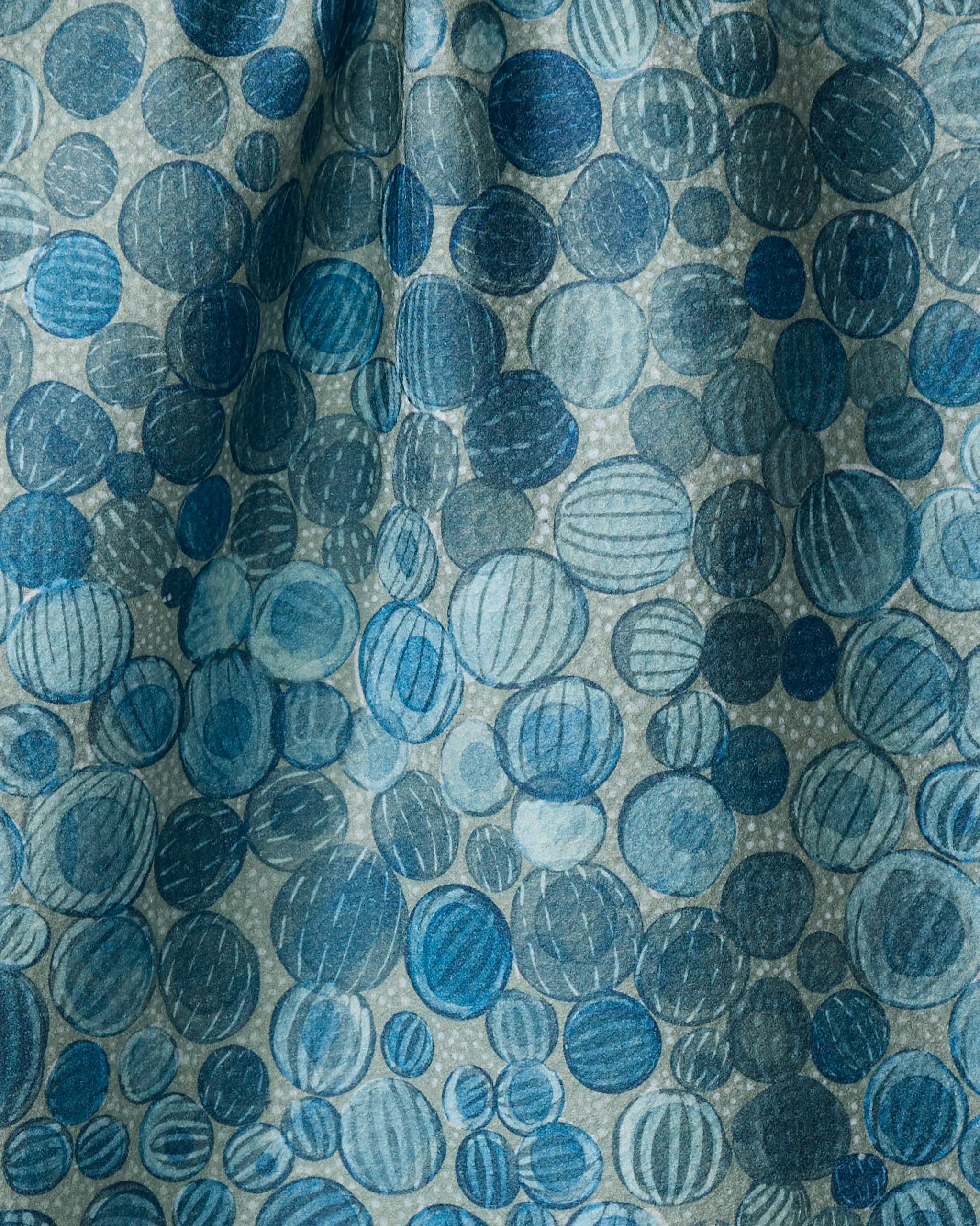 A close-up of Glass Baubles fabric by Katie O'Shea features blue and teal circles in varied sizes with textured lines, creating a playful, layered look—ideal for a quick-drying tea towel made from recycled materials.