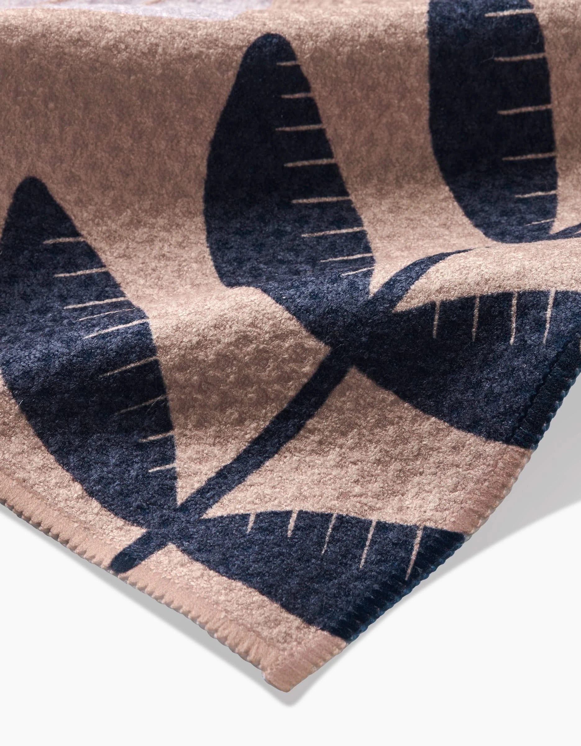 A close-up of the Gloria tea towel by Amy MacCready, made from post-consumer recycled Geoweave fabric with a beige background, dark blue leaf pattern, and stitched edges.