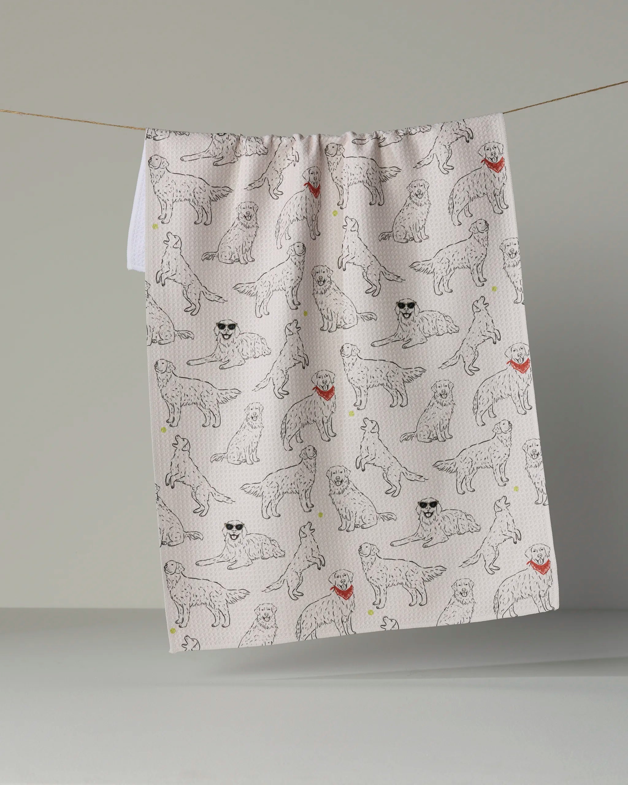 The “Golden Gang” tea towel by Geometry features black line drawings of dogs sporting red bandanas and sunglasses, hanging stylishly against a plain background to add playful charm to your kitchen. Eco-friendly and practical, this towel is the perfect accent for any home.