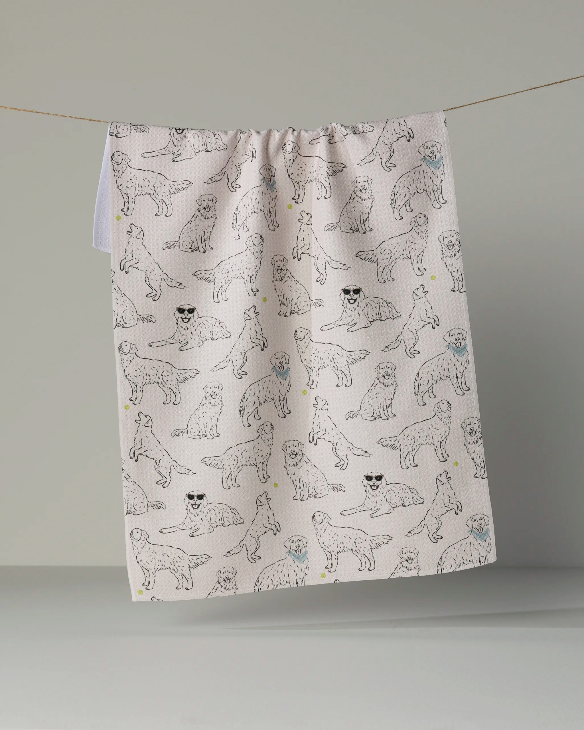 The Geometry “Golden Gang” tea towel features a stylish pattern of line-drawn dogs in various poses—some sporting playful sunglasses—and hangs on a clothesline against a plain, light-colored background. This eco-friendly towel from Geometry adds charm and character to any kitchen décor.