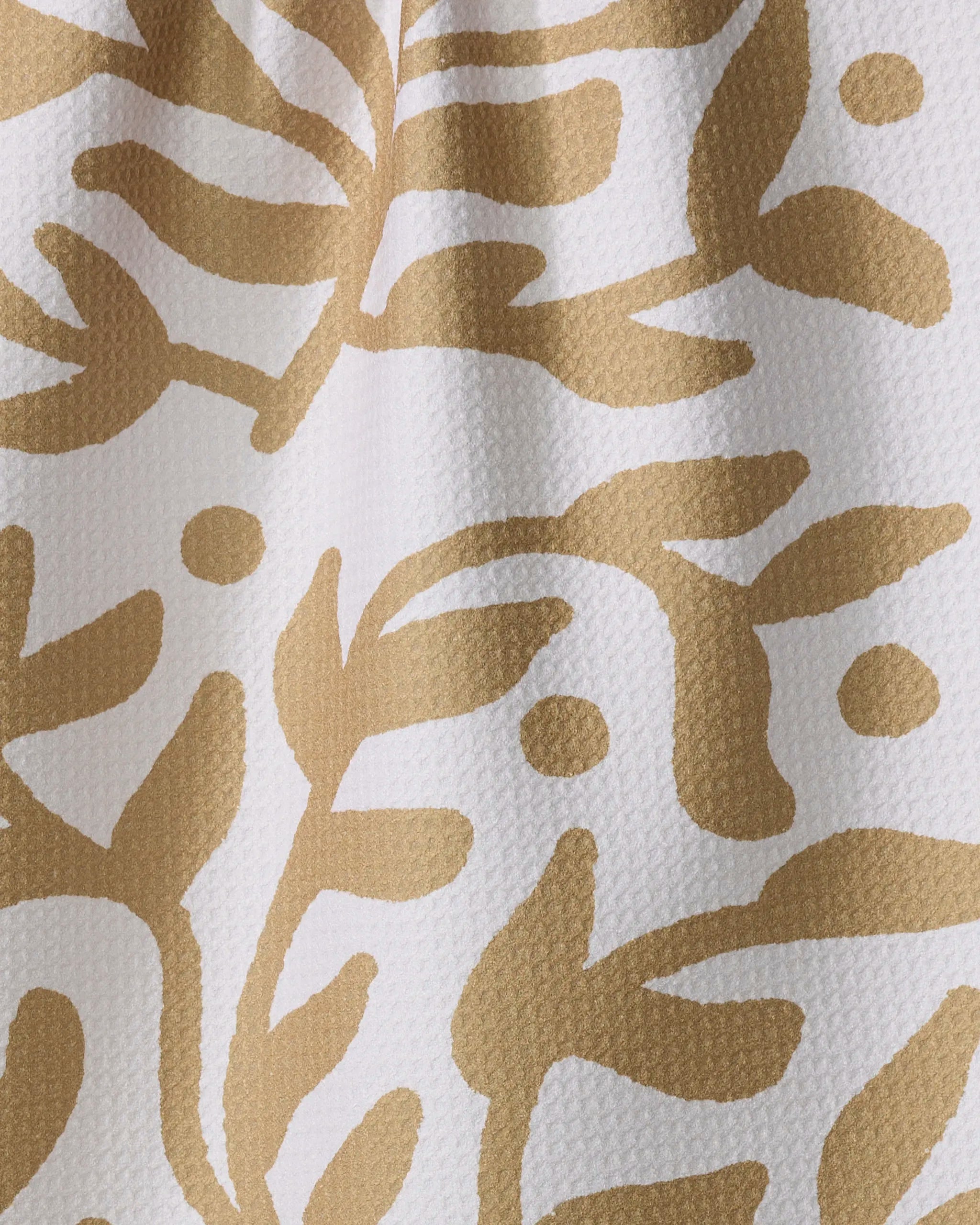 Close-up of textured white fabric from the Golden Garden ultra-absorbent towel by Graphics and Grain, featuring a mustard yellow abstract leaf and vine pattern with curved lines and dots, partially shadowed.
