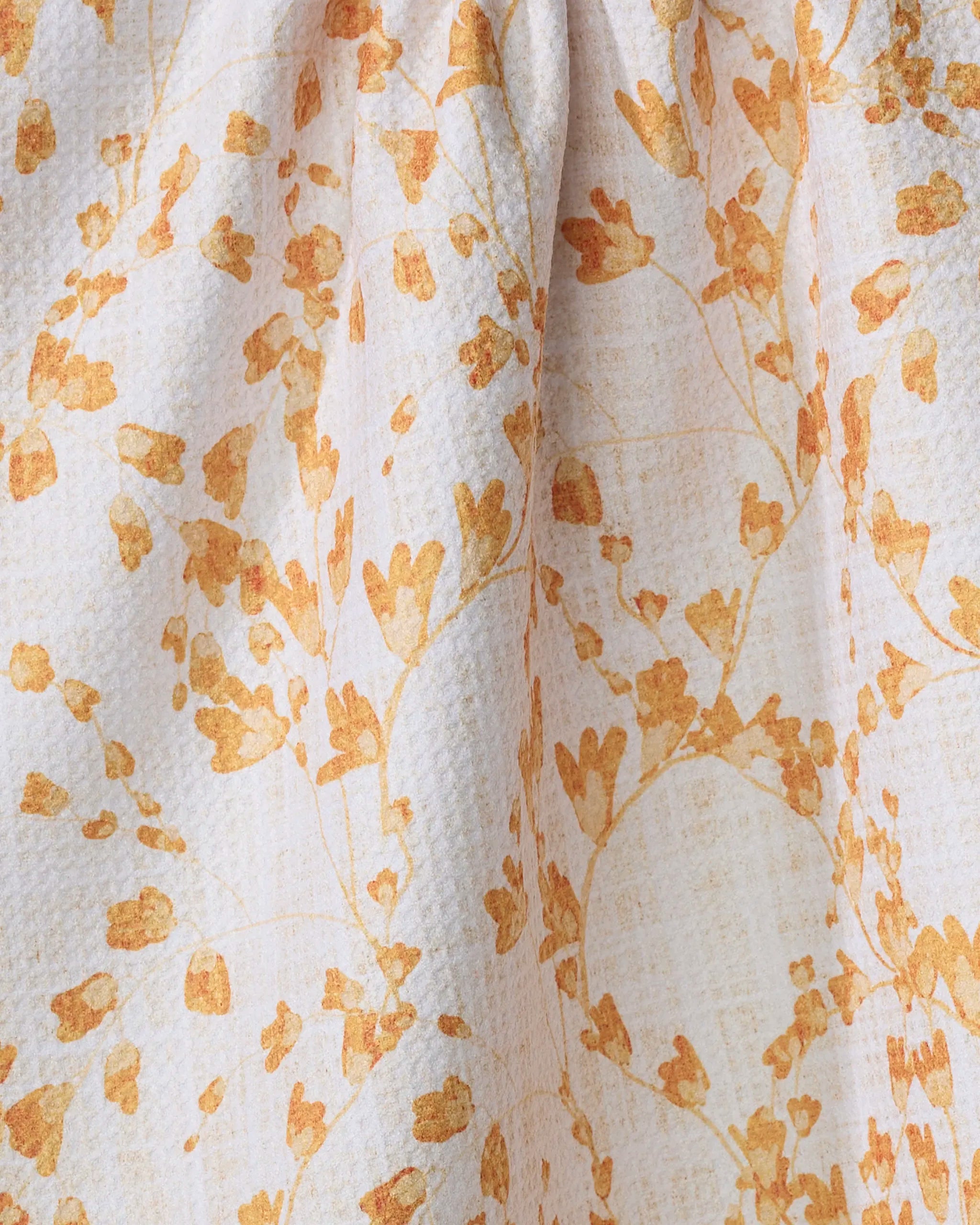 Close-up of Pascale Dilger’s Golden Grassland tea towel, featuring textured white fabric with yellow and orange floral branches. Made from quick-drying recycled materials for a soft, nature-inspired look and added convenience.