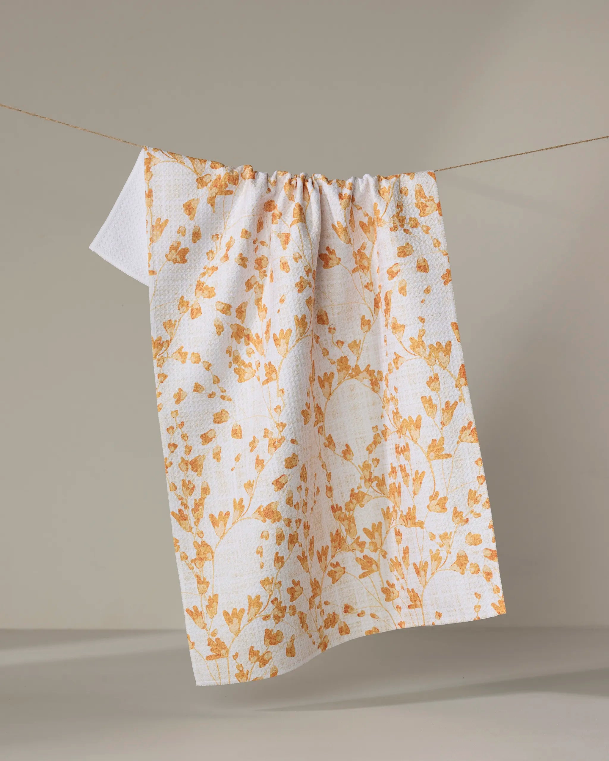 The Pascale Dilger "Golden Grassland" recycled kitchen towel, featuring a yellow floral pattern, hangs on a clothesline against a neutral background.