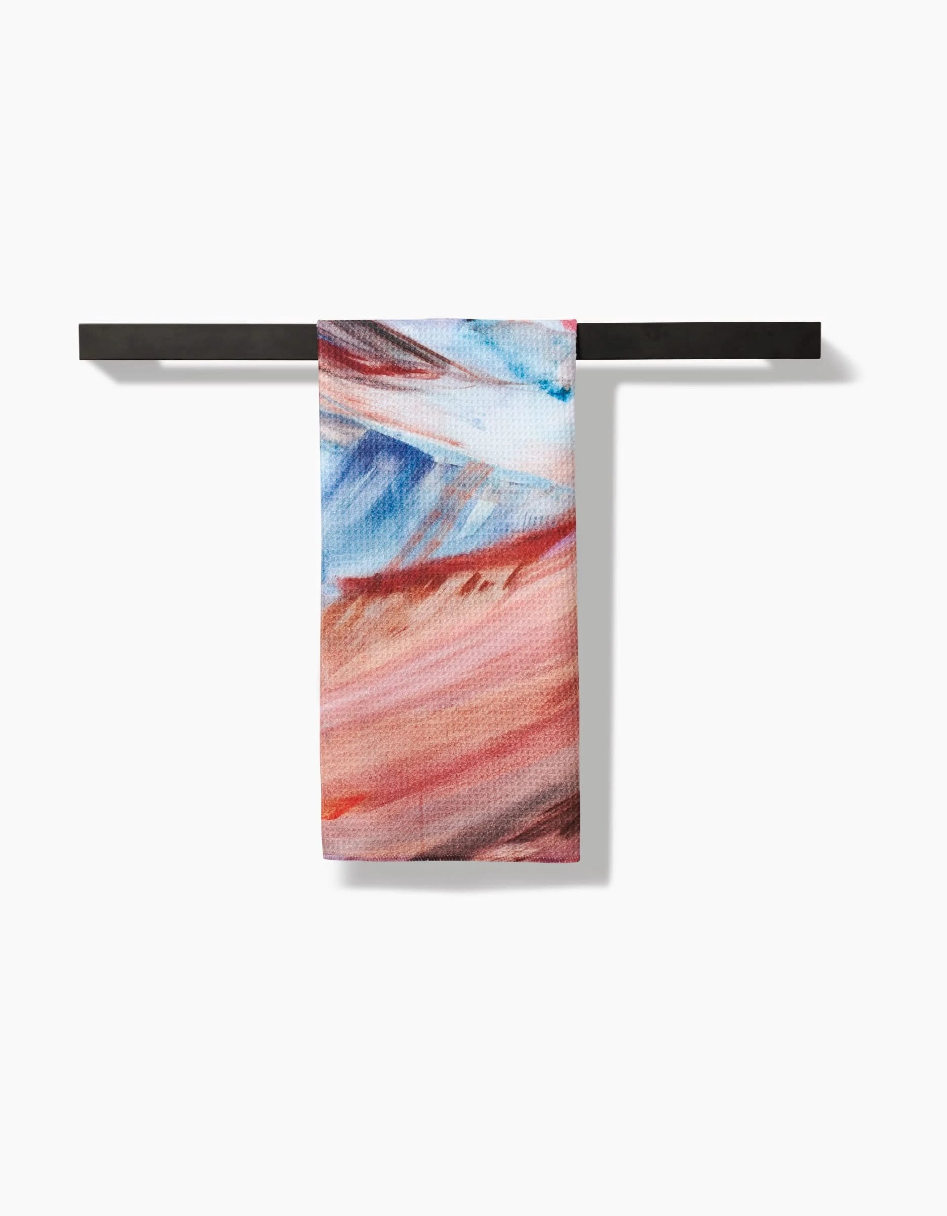 The Golden Hour in the Rockies towel by Kelly Peters, featuring an abstract red, blue, and white design, hangs on a black bar. Made from ultra-absorbent Geoweave fabric for superior performance against a white background.