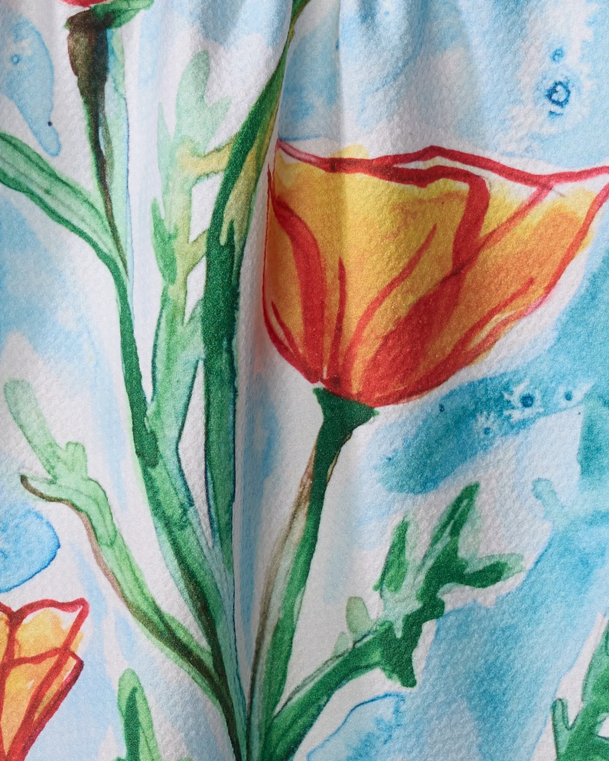 Golden Poppy Flowers" by Skye Walker features orange and yellow blooms with green stems on a light blue background, painted in soft watercolor brushstrokes on textured paper—evoking the charm of a vintage tea towel.