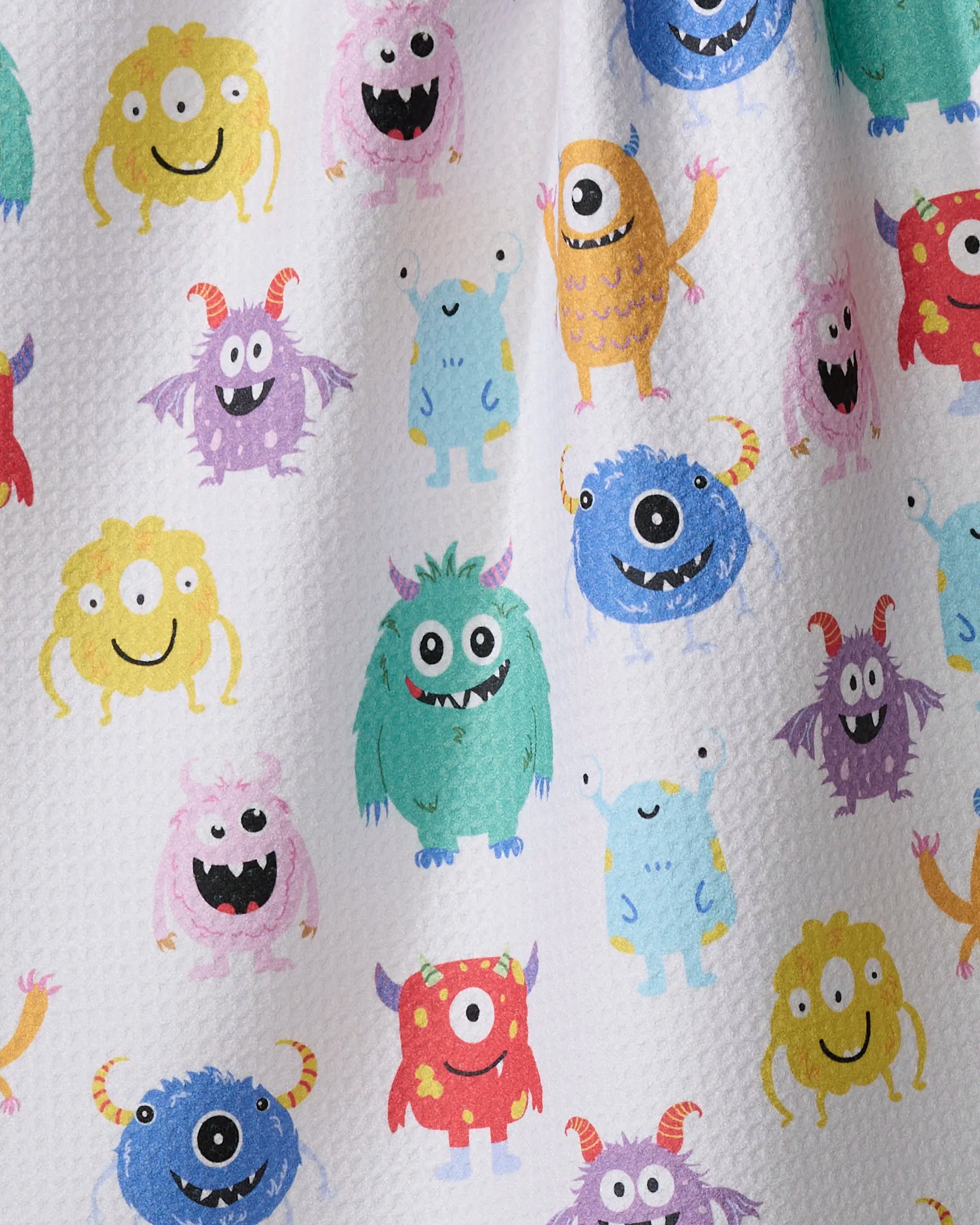 The "Goofy Critters" tea towel by Vaishali Design Studio features playful blue, green, yellow, pink, purple, and orange cartoon monsters on white textured fabric made from recycled materials. Ultra-absorbent and fun!.