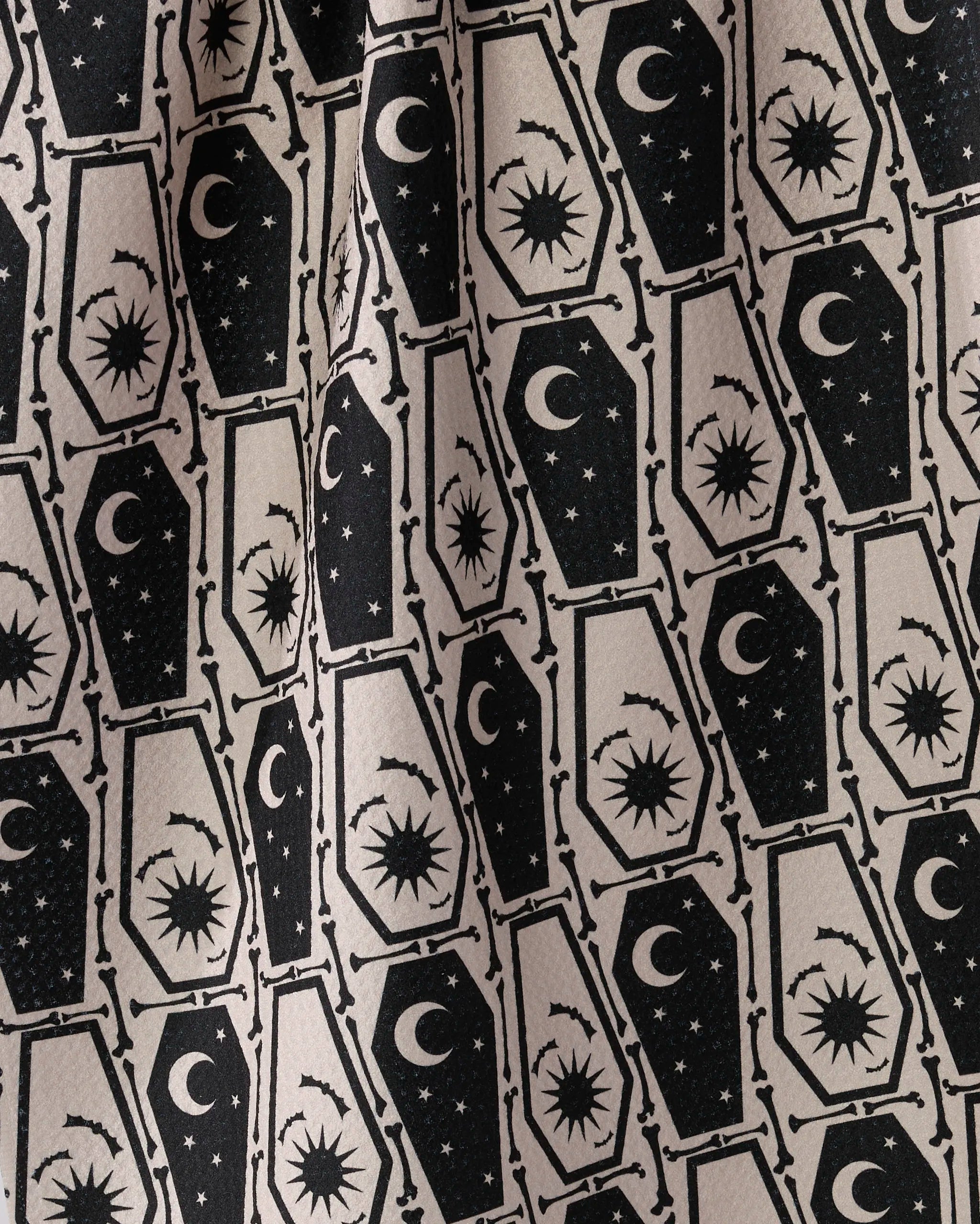 The Geometry "Gothic Slumber" tea towel features black coffins with celestial designs on a beige background, arranged in alternating directions—an eye-catching addition to any kitchen.