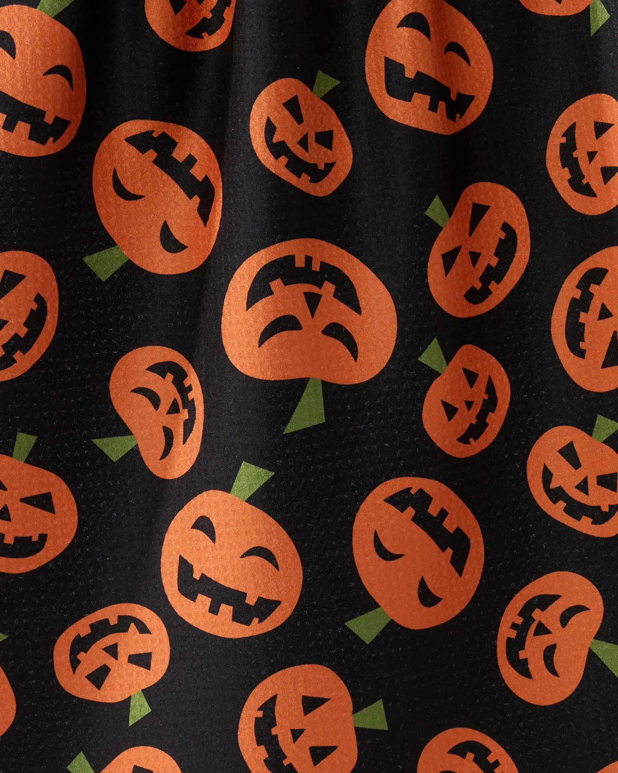 Gourd Gang by Geometry features orange jack-o-lantern faces with spooky expressions and green stems on black fabric—perfect for a festive tea towel made from recycled materials.