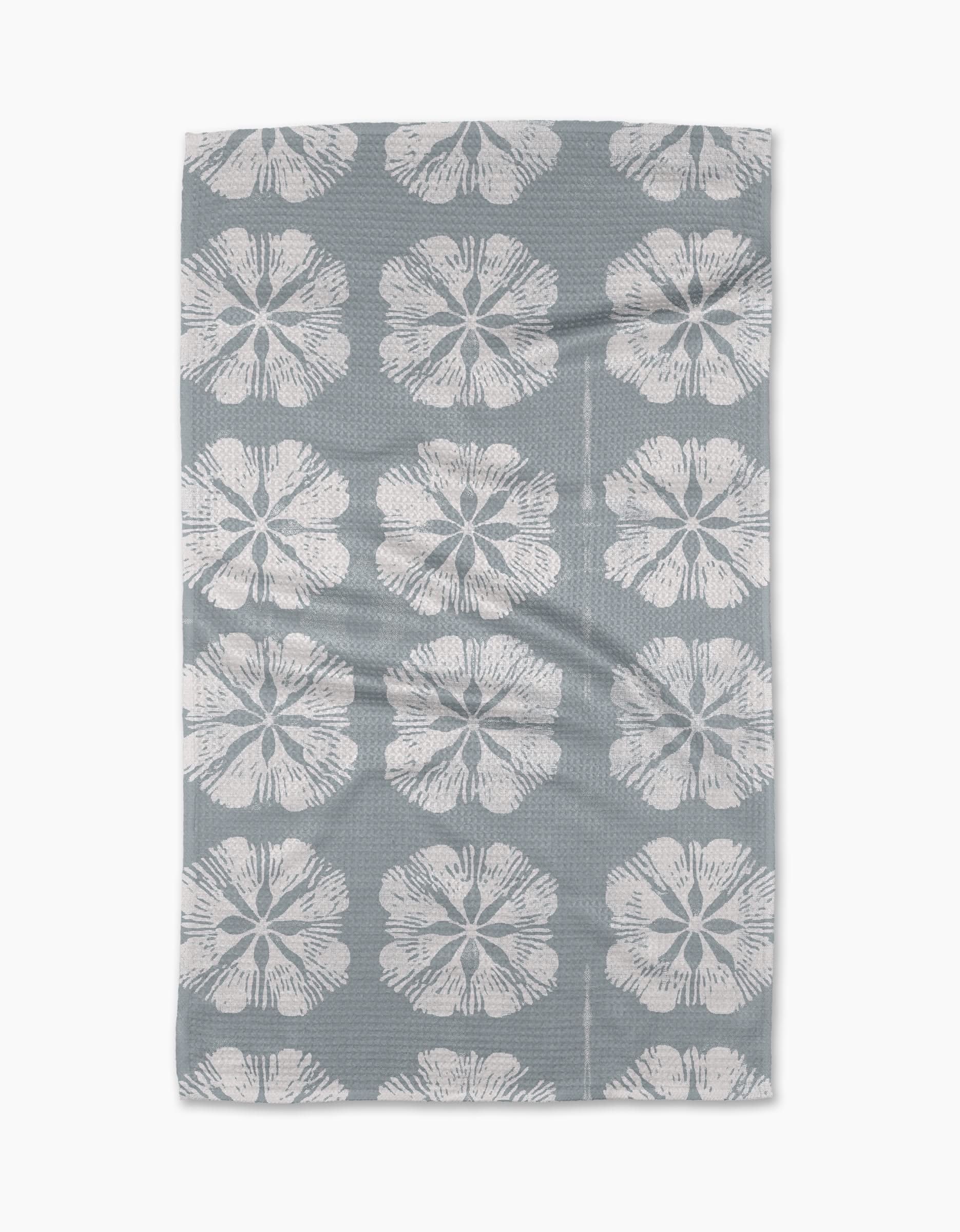 The Geometry Gracie Tea Towel is rectangular and grey, with large white stylized flowers in neat rows. Made from Geoweave fabric, the towel lies flat with slight folds visible.