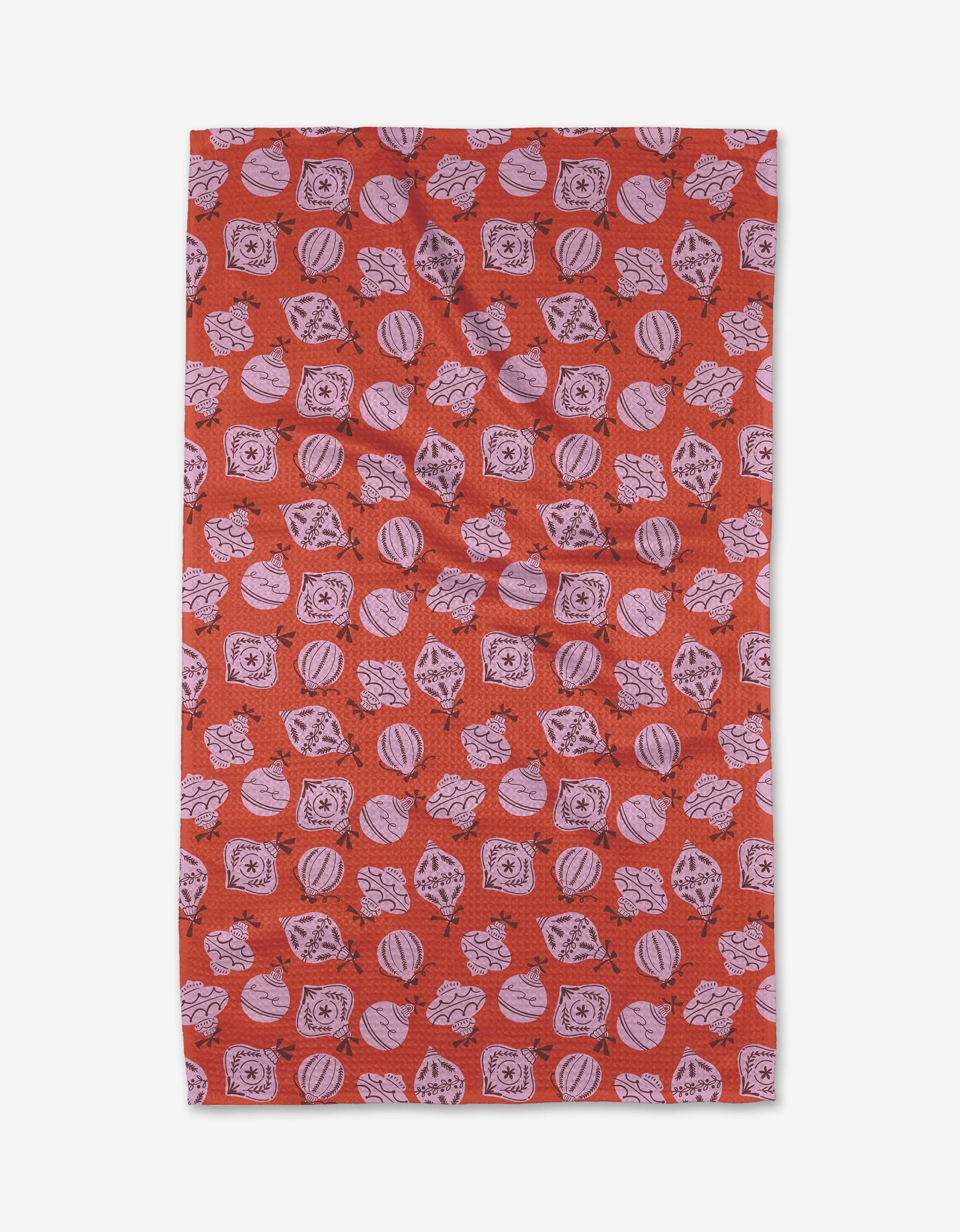 The Grams Ornaments tea towel by Charlie Rowan Designs is a red rectangular towel with an all-over pattern of pink Christmas ornaments, holly leaves, and square shapes, made from quick-drying recycled materials.