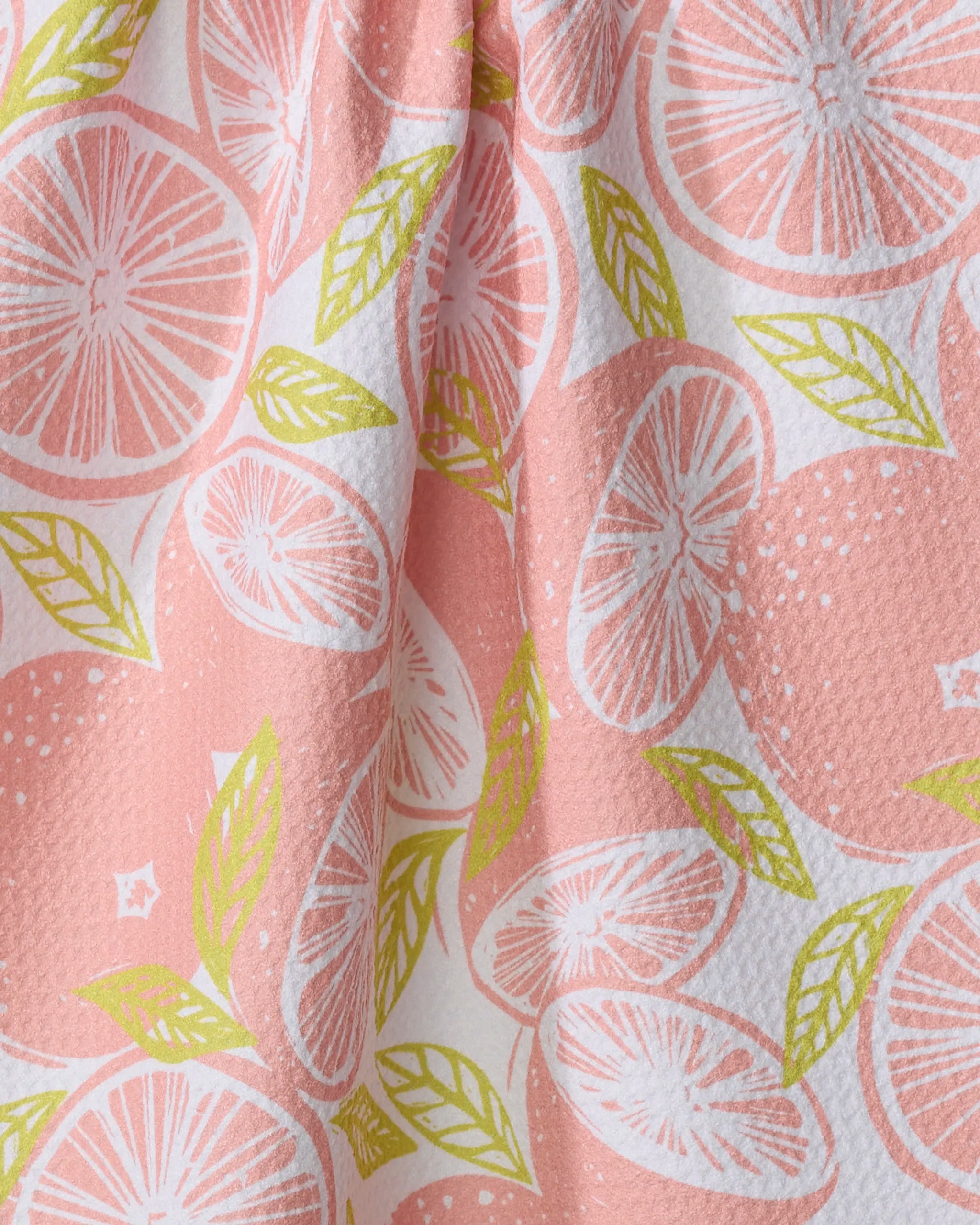 A close-up of Elisabeth Wing's "Grapefruits" fabric shows pink recycled material with sliced citrus and green leaves—perfect for a vibrant kitchen towel, featuring textured detail and white highlights.