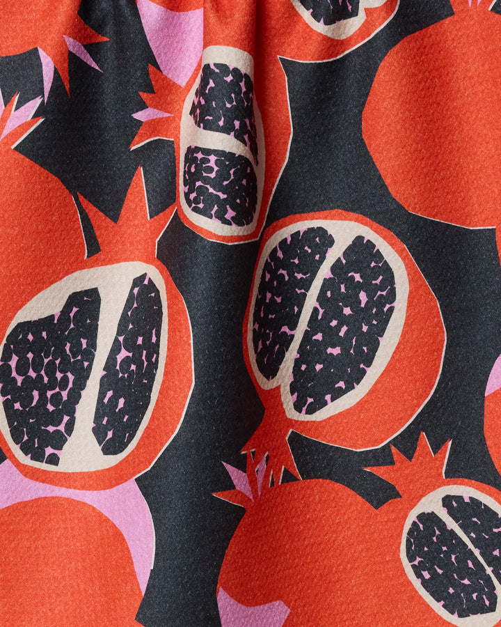 The Claire Iglesias "Graphic Pomegranates" tea towel is made from recycled materials and displays bold, colorful pomegranate designs—whole and halved—on a striking black background.