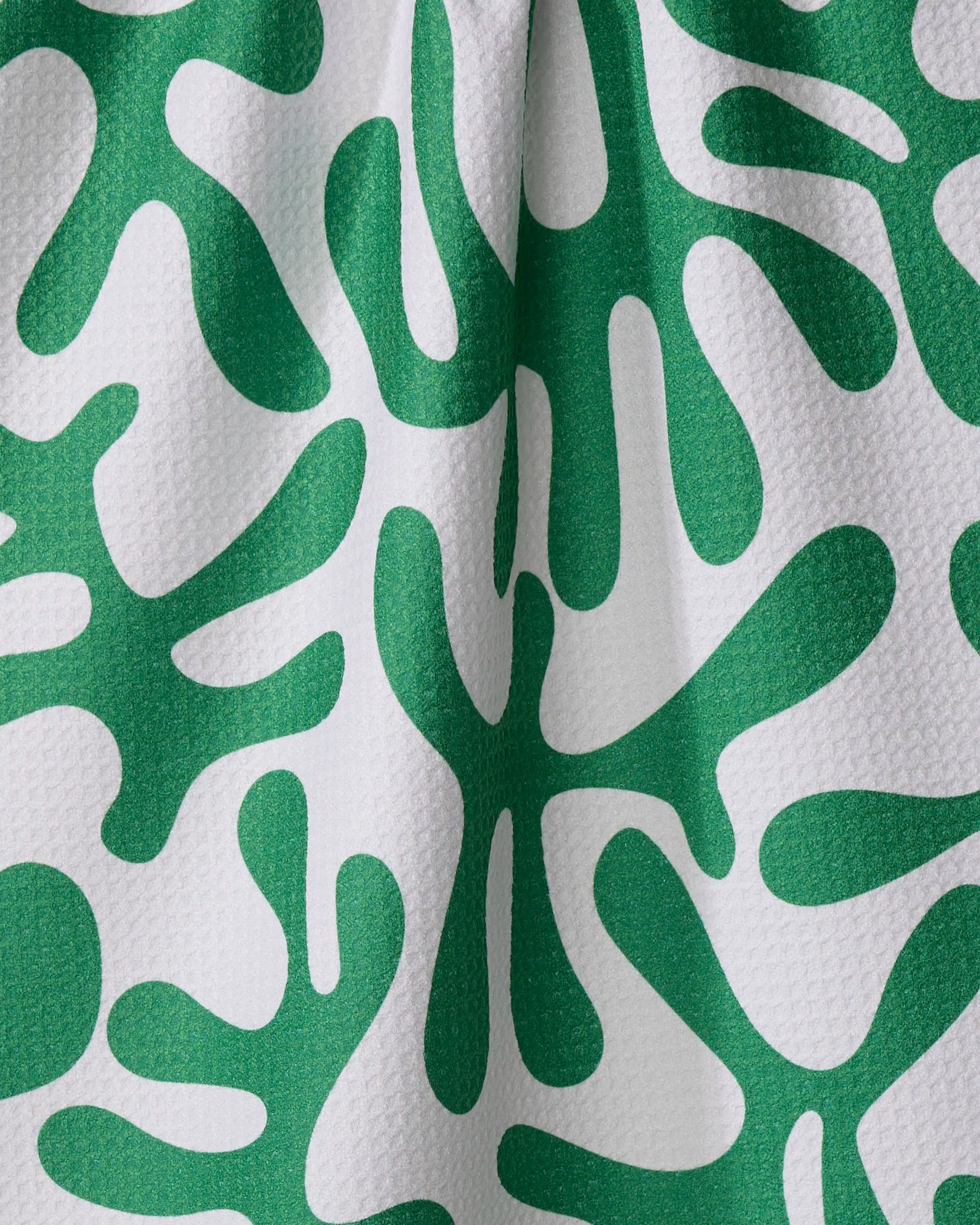 Marina Solodka’s Green Afternoon tea towel features green abstract, coral-inspired shapes on a textured white surface with small raised dots. Made from recycled materials, subtle folds add shadow and depth.