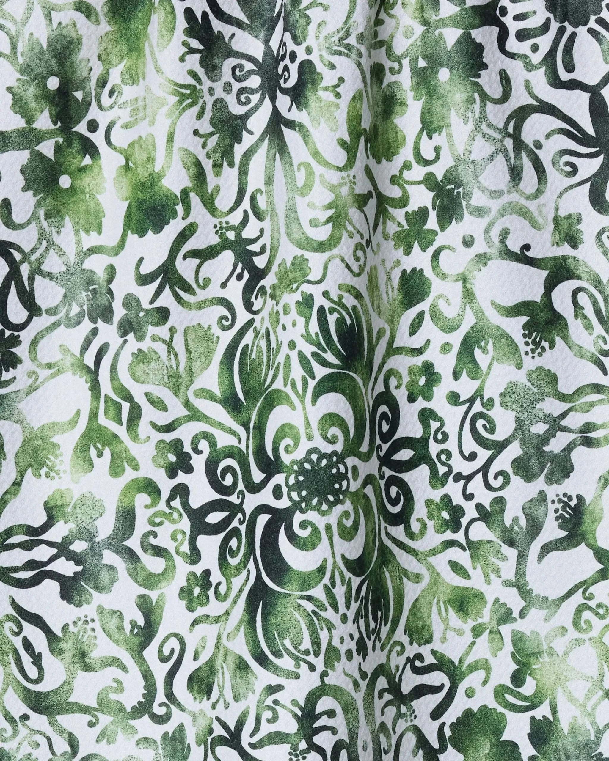 The Geometry Green Goddess kitchen towel features green and black floral and leafy patterns on white textured recycled fabric, creating a symmetrical, decorative look.