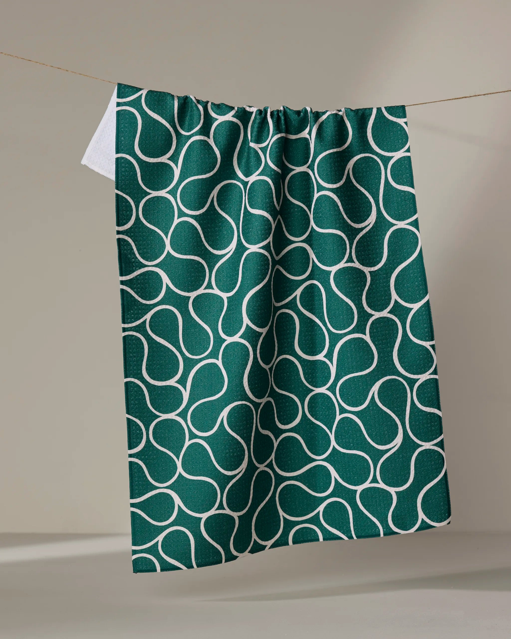 The Gerdadzy Green Loops towel, ultra-absorbent and dark green with a white curvy interconnected line pattern, hangs on a clothesline against a neutral background.