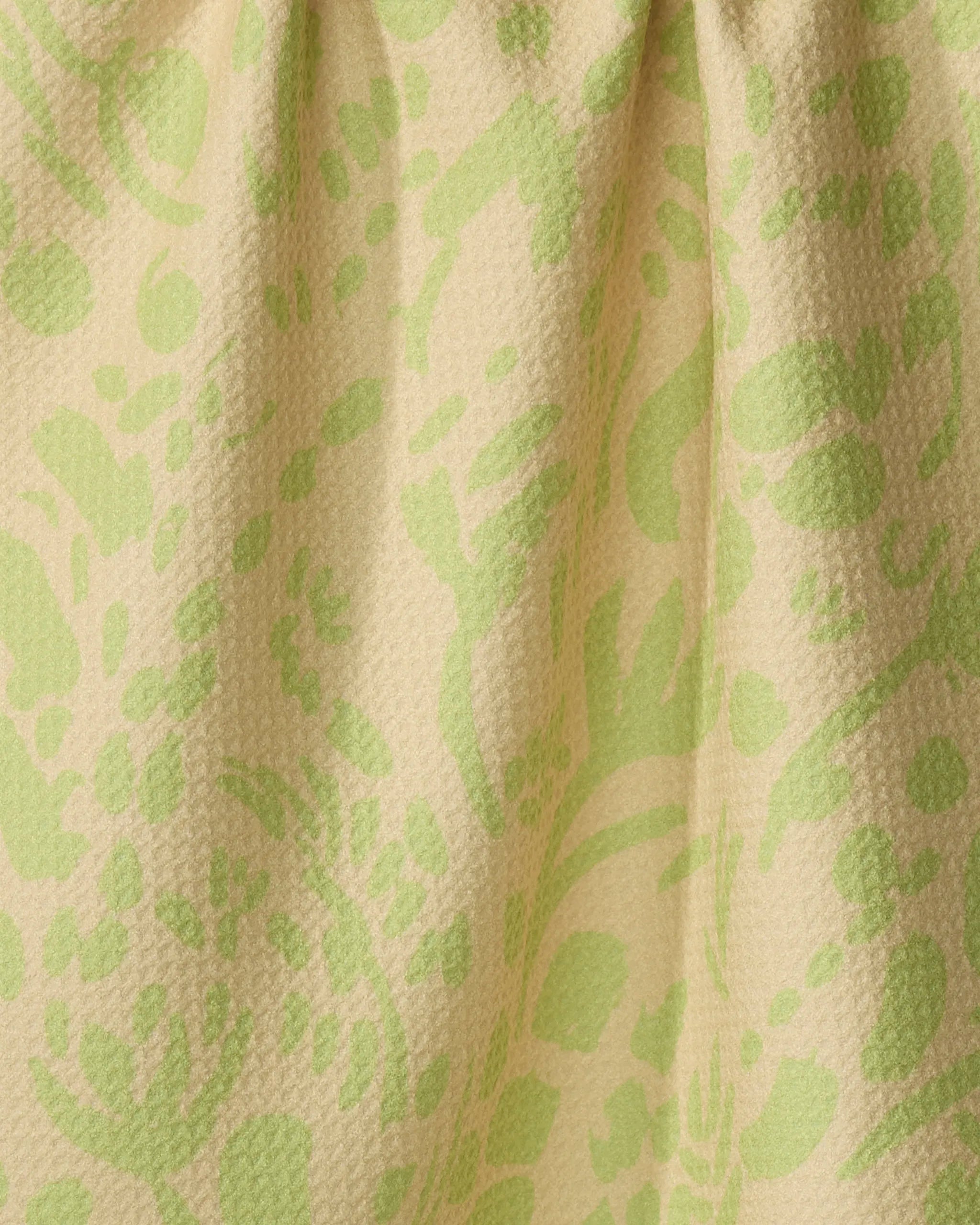 Close-up of Sareka Unique’s Green Spring tea towel, featuring a yellow-beige background with light green floral patterns. Made from recycled materials, the fabric is slightly gathered at the top.