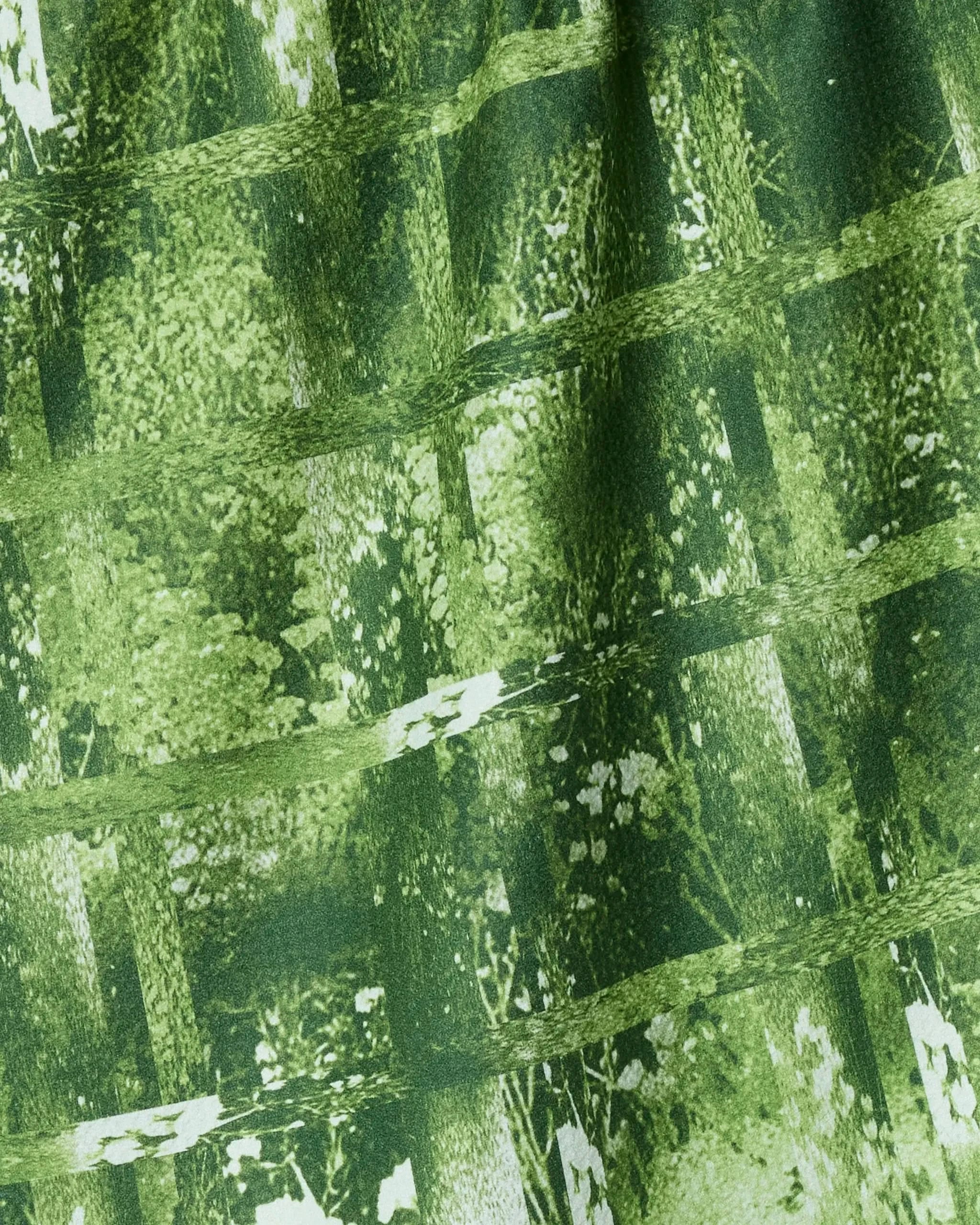 Close-up of Geometry's Greenhouse tea towel, ultra-absorbent and made from recycled materials, featuring a green grid over abstract foliage and tree designs in light and dark green tones.