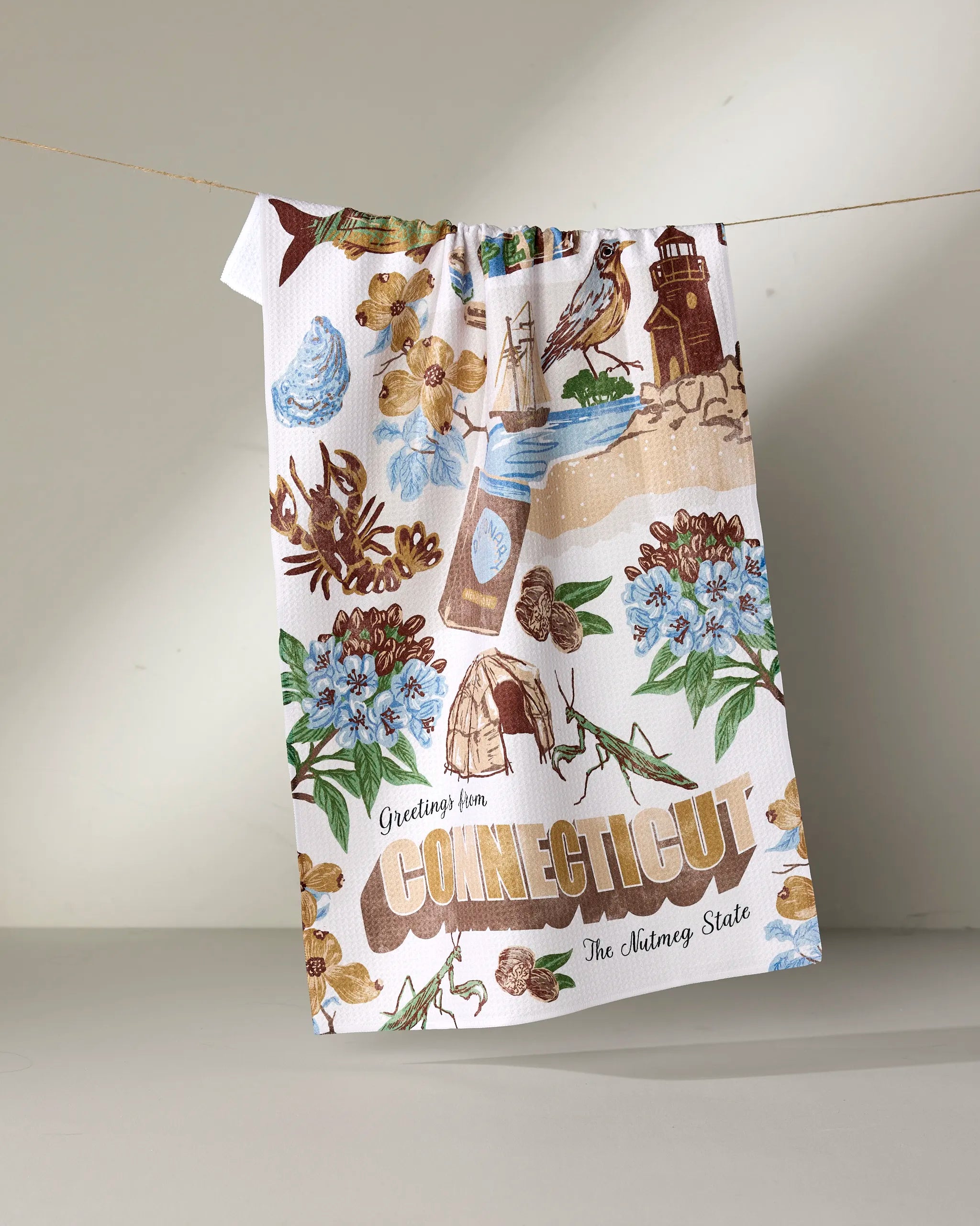 The Geometry "Greetings From Connecticut" tea towel features illustrations of state symbols and “Greetings from Connecticut” with “The Nutmeg State” text, made from ultra-absorbent kitchen towel material.