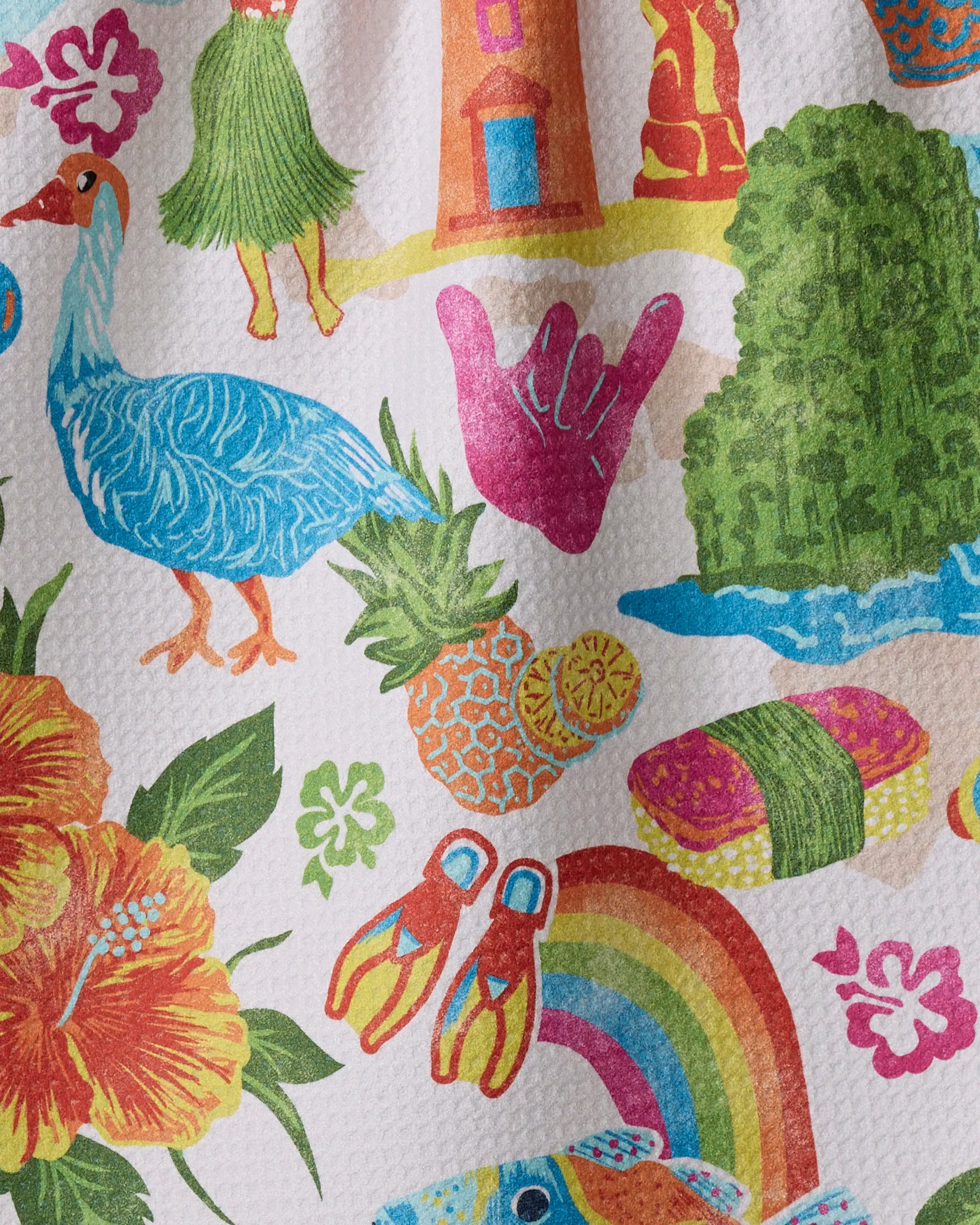The Geometry "Greetings From Hawaii" kitchen tea towel features a vibrant, ultra-absorbent design with a blue goose, hibiscus, sushi, pineapples, shaka hand sign, swim fins, rainbow, waves, and tropical elements on a textured background.