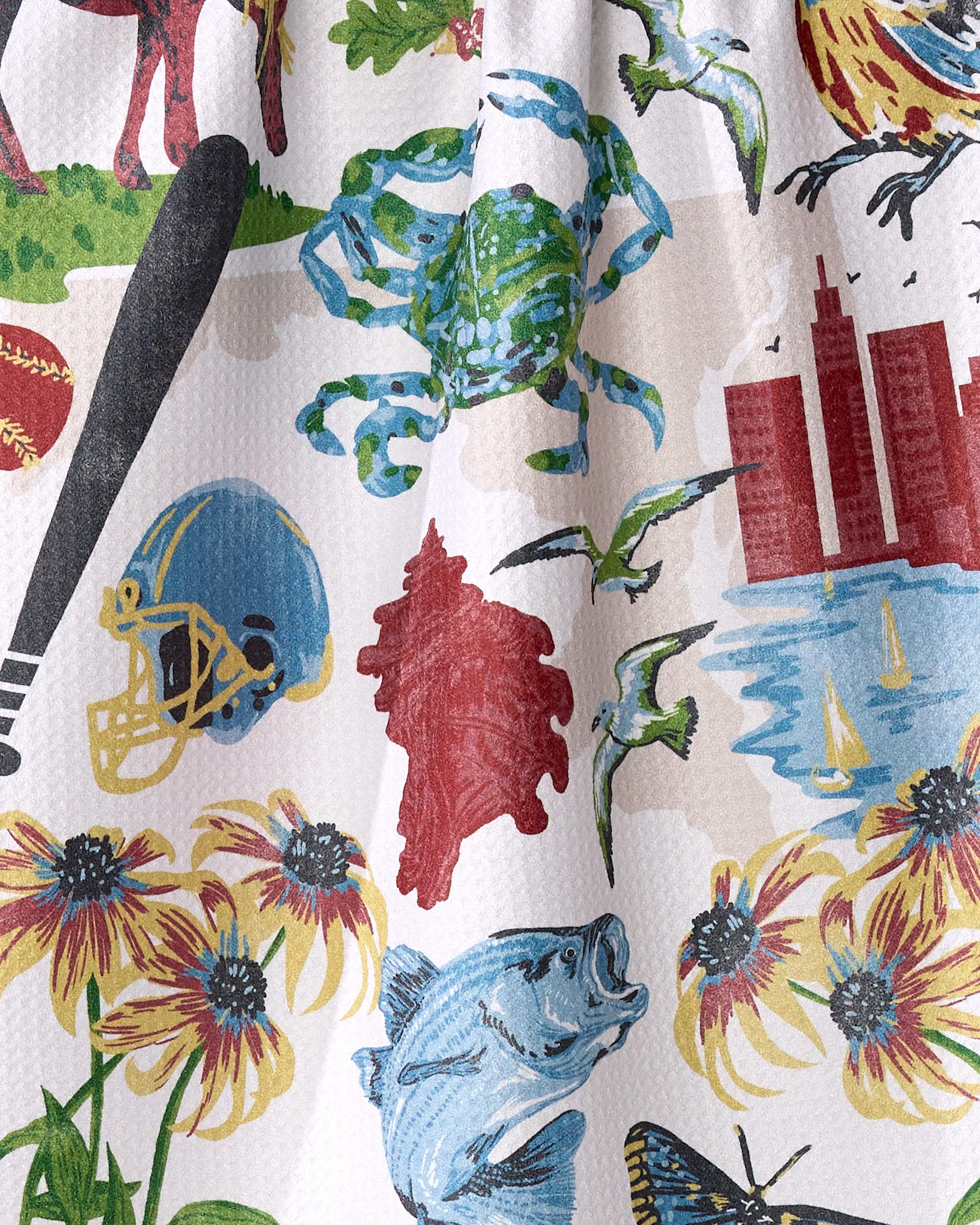 The "Greetings From Maryland" tea towel by Geometry showcases a vibrant pattern with a crab, football helmet, baseball bat, skyscrapers, birds, fish, flowers, and butterfly on white—ultra-absorbent and made from recycled materials.