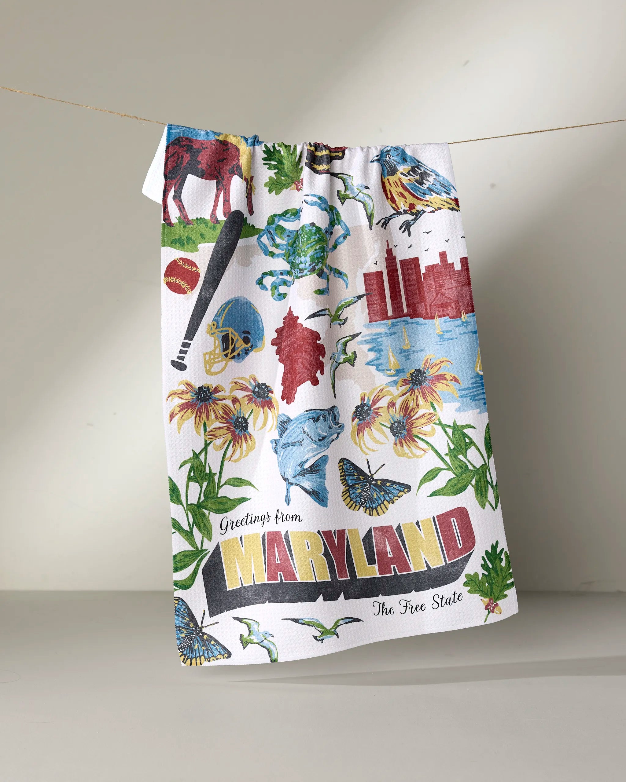 The Geometry “Greetings From Maryland” tea towel is ultra-absorbent and features vibrant illustrations of local icons like a crab, black-eyed Susans, the Baltimore Oriole, state flag, and the phrase “Greetings from MARYLAND The Free State.”.