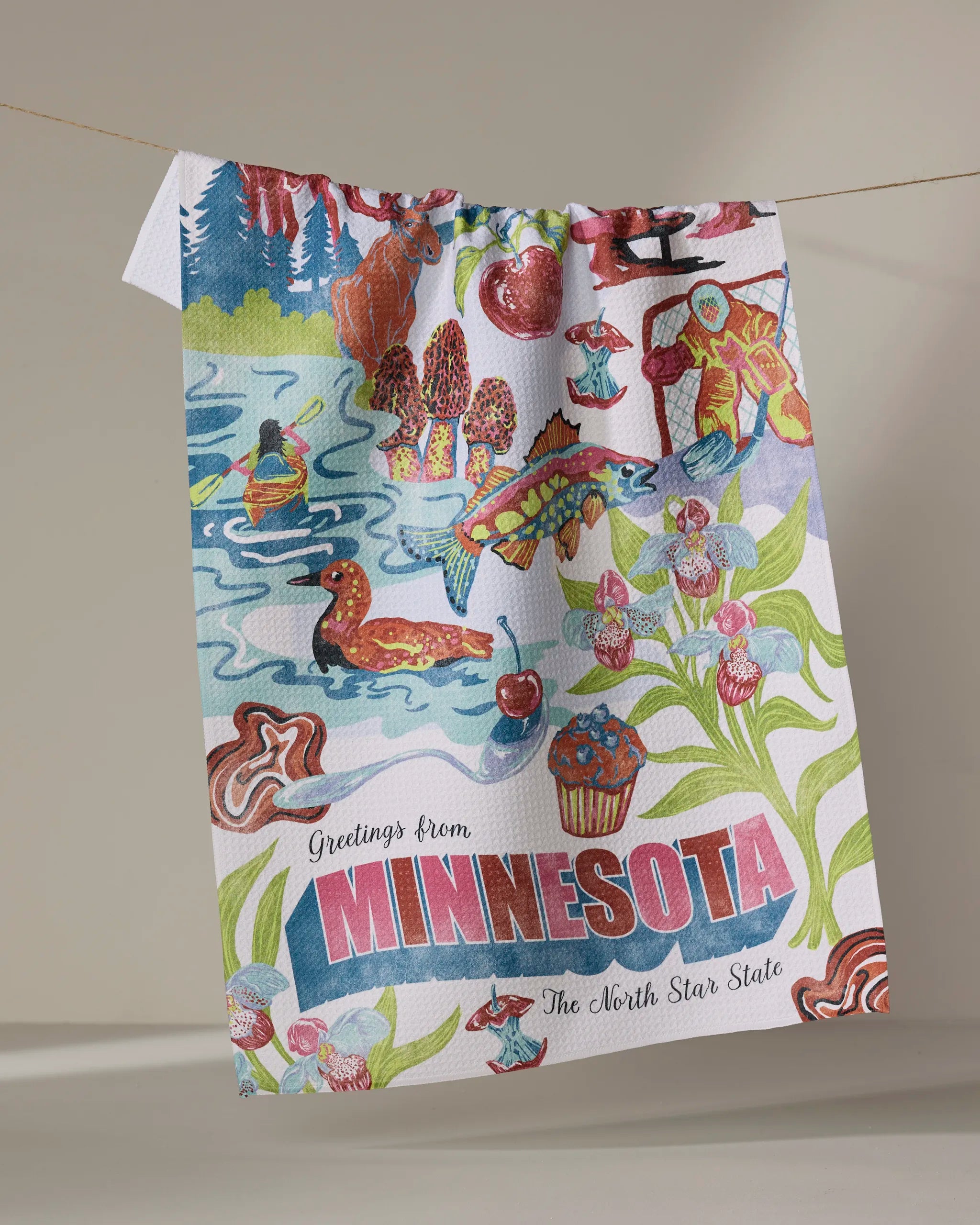 Geometry’s “Greetings From Minnesota” tea towel features vibrant illustrations of state symbols and “Greetings from MINNESOTA The North Star State” text. Made from recycled materials.