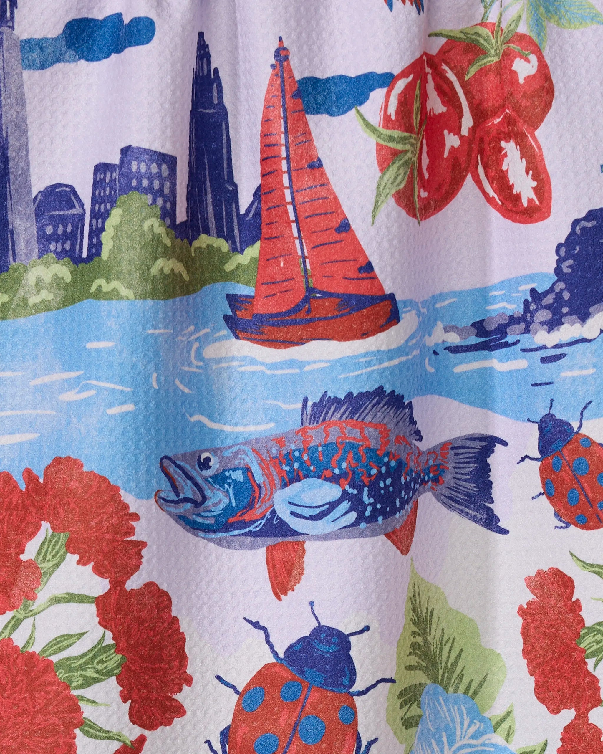 The "Greetings From Ohio" recycled kitchen towel by Geometry features colorful patterns: a red sailboat on water, a blue and red fish, ladybugs, tomatoes, red flowers, and a city skyline backdrop.