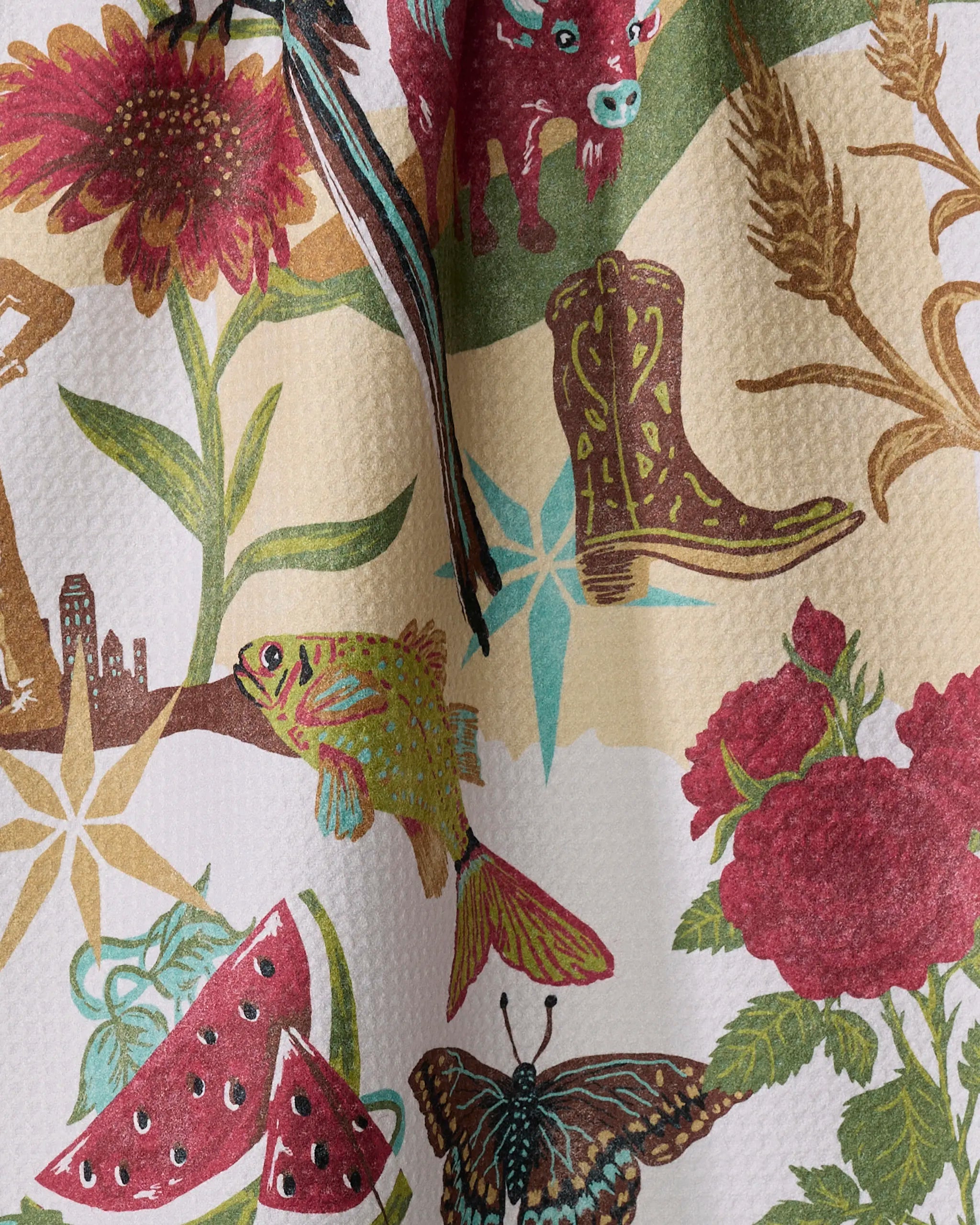 The Geometry "Greetings From Oklahoma" tea towel is made from recycled materials and features earthy-toned illustrations of a cowboy boot, fish, watermelon slices, butterfly, roses, sunflower, wheat, longhorn steer, and a city skyline.