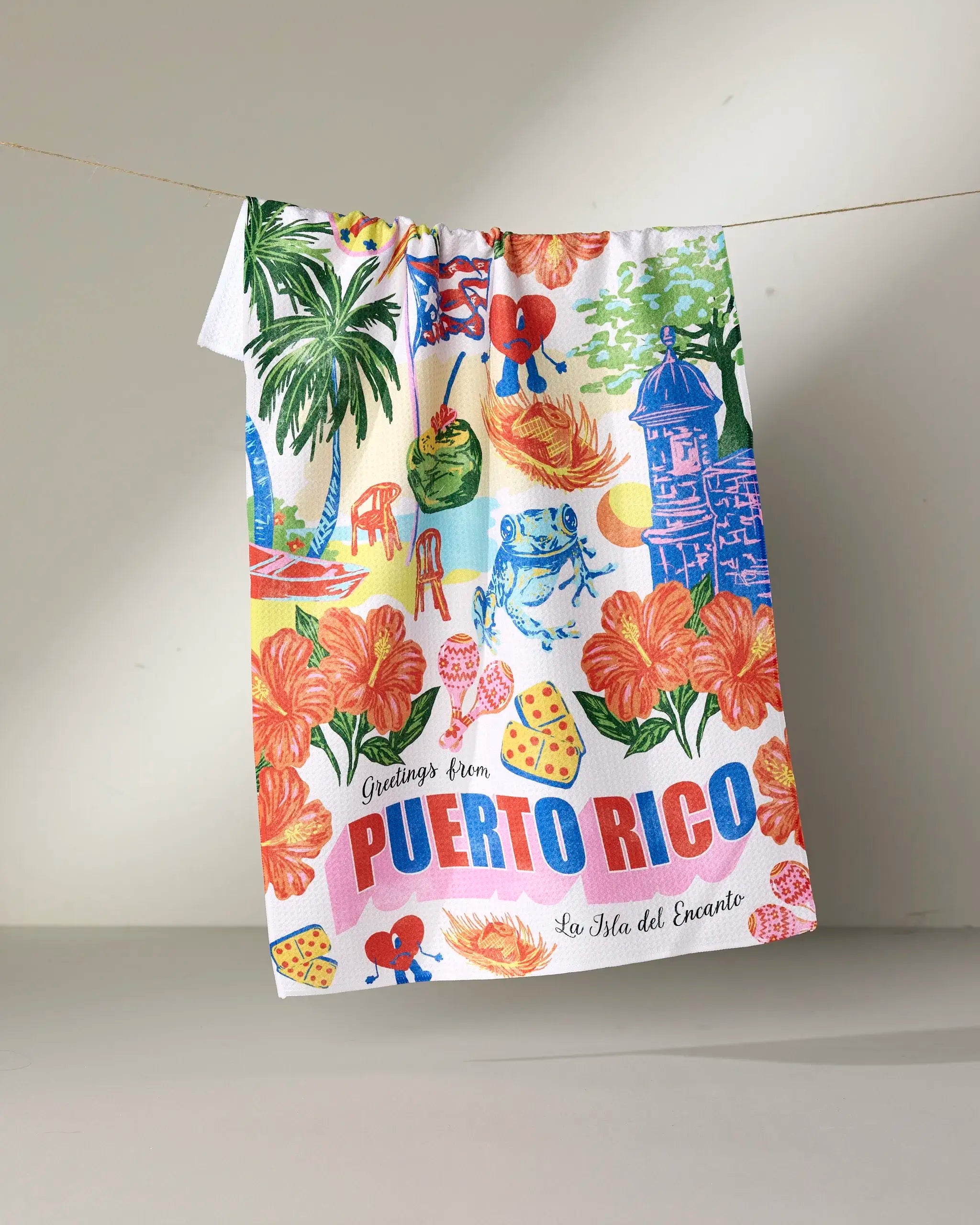 The Geometry Greetings From Puerto Rico tea towel features vibrant tropical designs with hibiscus flowers, a frog, palm trees, fruits, and bold "Greetings from Puerto Rico, La Isla del Encanto" text. Quick-drying and colorful for your kitchen.