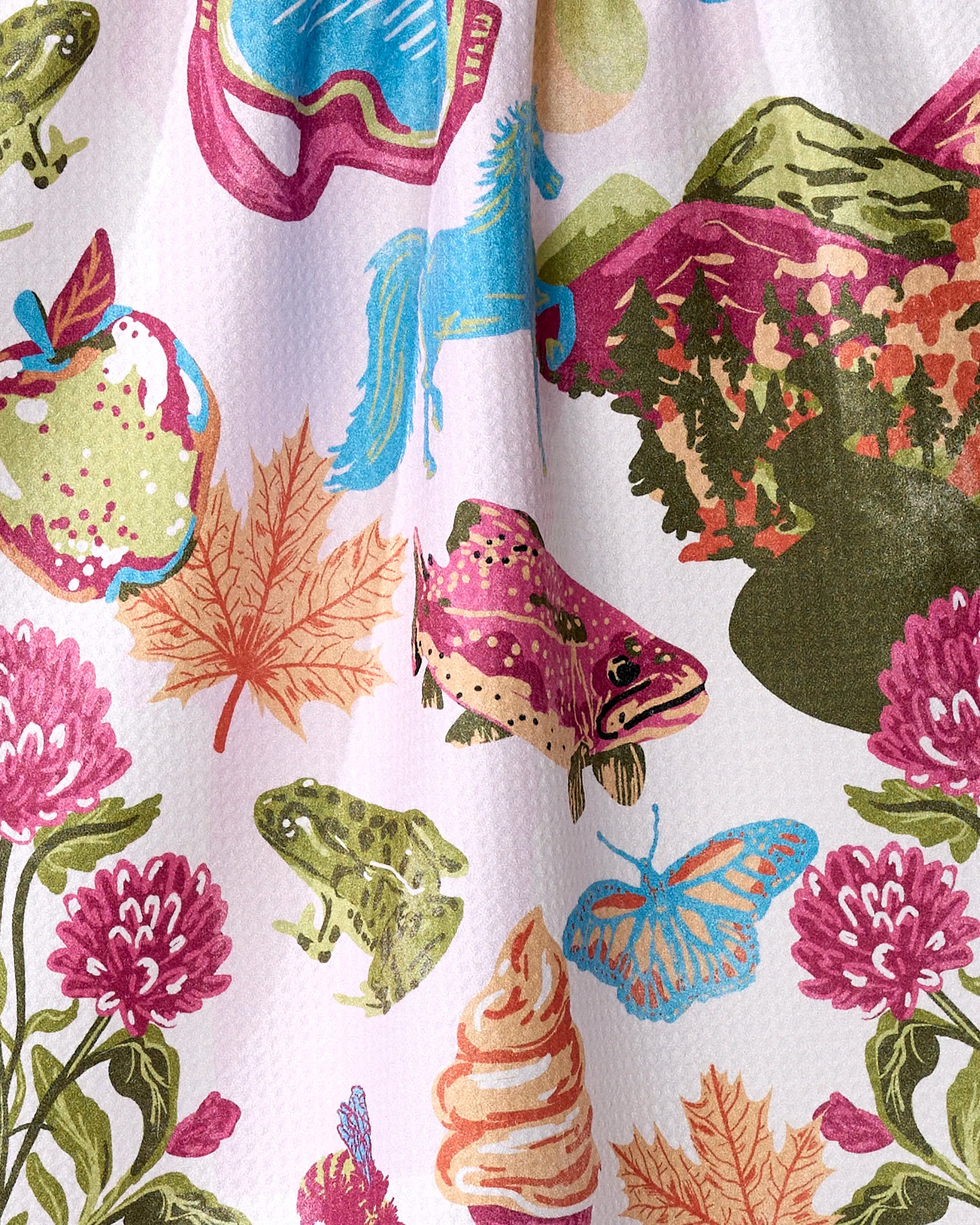 The Geometry "Greetings From Vermont" tea towel features vibrant illustrations of apples, frogs, a trout, and mountains in pinks, greens, and blues—crafted from recycled materials.