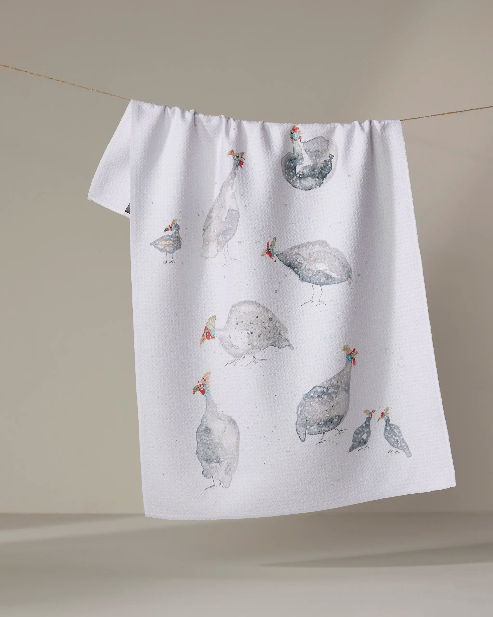 The "Guinea Fowls" tea towel by Taryn Brennan features watercolor guinea fowl illustrations on a plain light background. Made from quick-drying recycled materials, it hangs perfectly for display or everyday use.