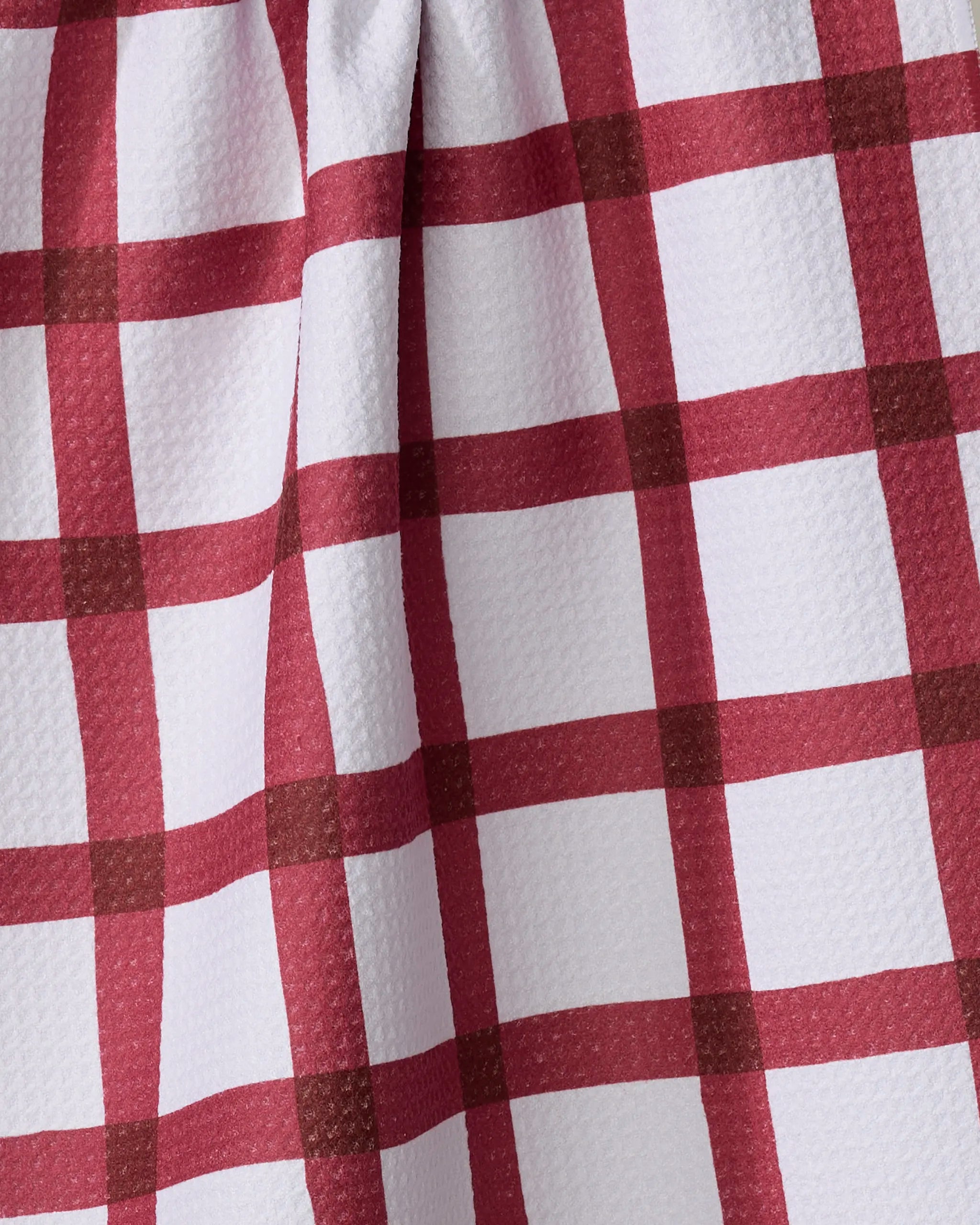Close-up of the Hackett tea towel by Amy MacCready, showing its textured white fabric with a red and burgundy plaid checkered pattern, gentle folds, and eco-friendly construction from recycled materials.