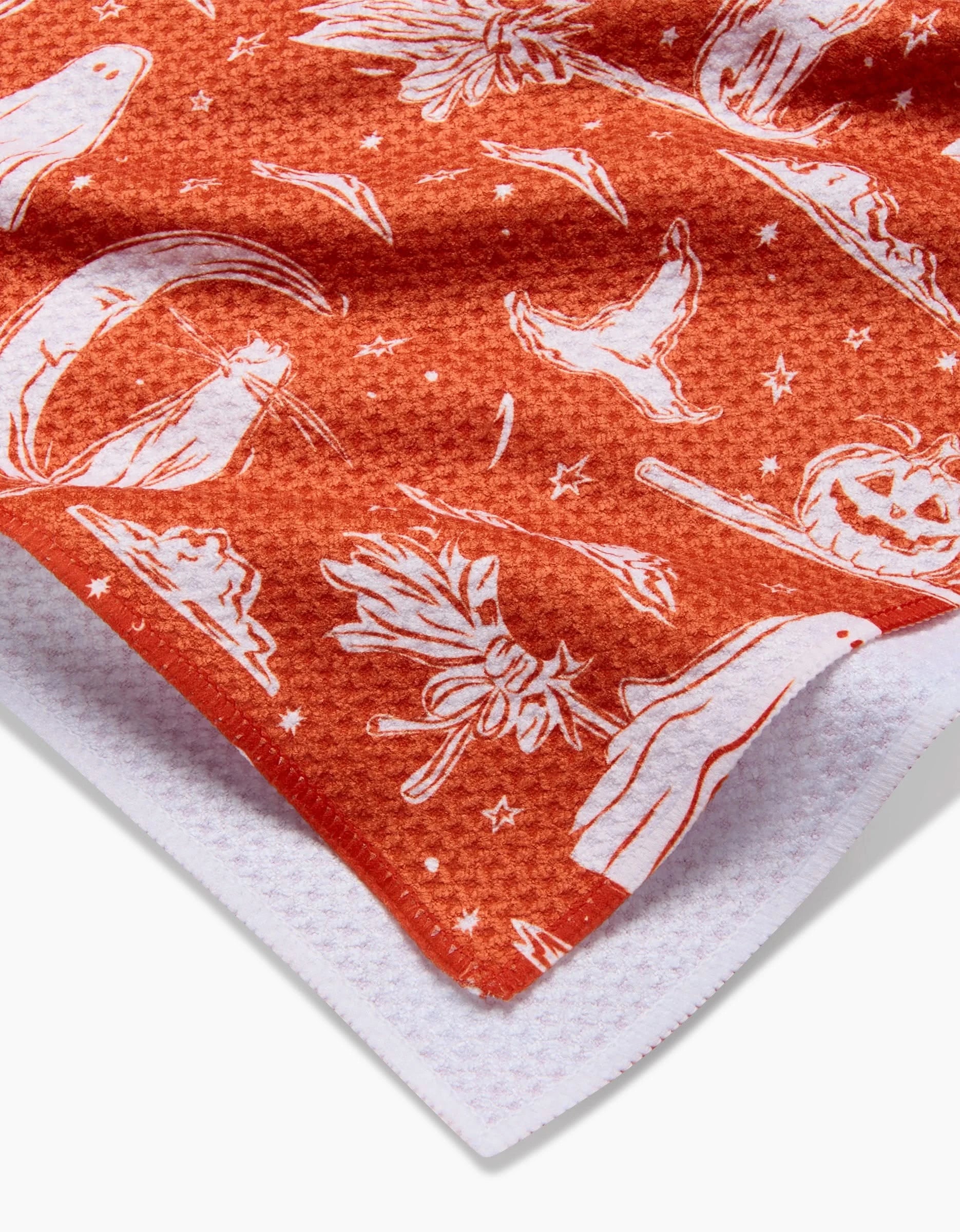 A close-up of the Halloween Cats And Ghosts towel by Aubrey Fairchild shows orange Geoweave™ fabric with white Halloween-themed illustrations. The ultra-absorbent towel features a textured surface, a white underside, and festive cat and ghost motifs.
