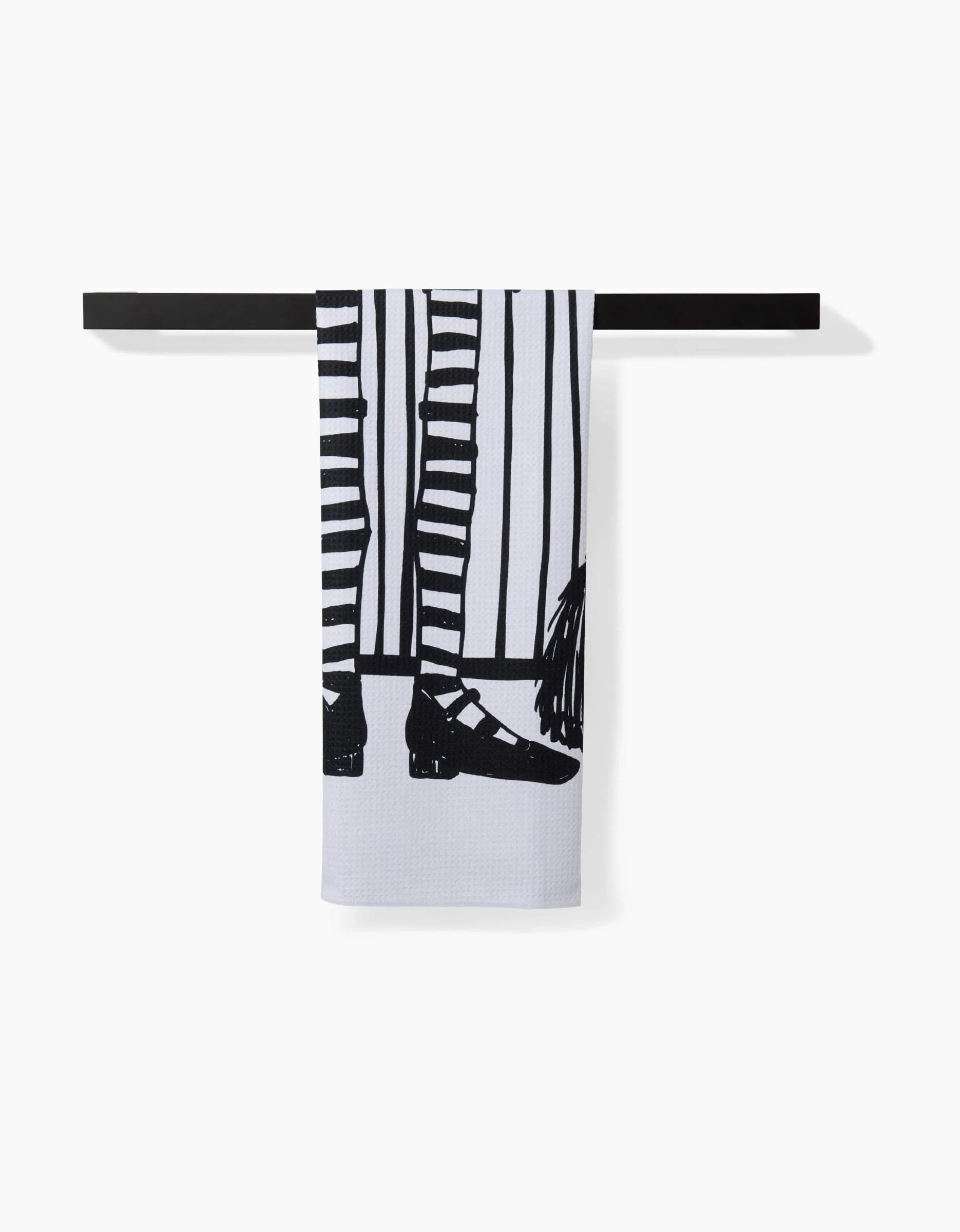The Hufton Studio Halloween Witch Legs tea towel features black illustrated legs in striped stockings and black shoes, hanging on a black towel bar against a white background. Quick-drying and stylish for your kitchen.
