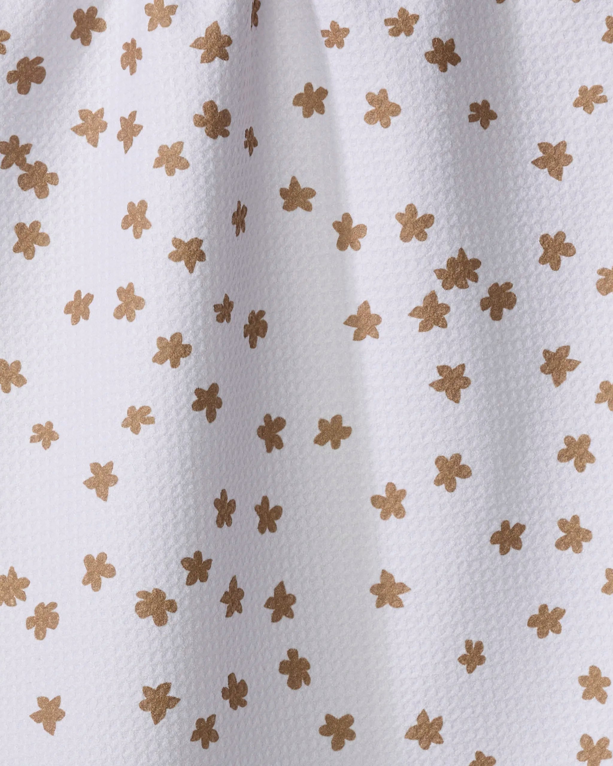 The Julianne Haness Haness Golden dish towel features white textured fabric with evenly spaced, small light brown floral shapes. Its absorbent design and gentle folds add a touch of elegance to your kitchen.