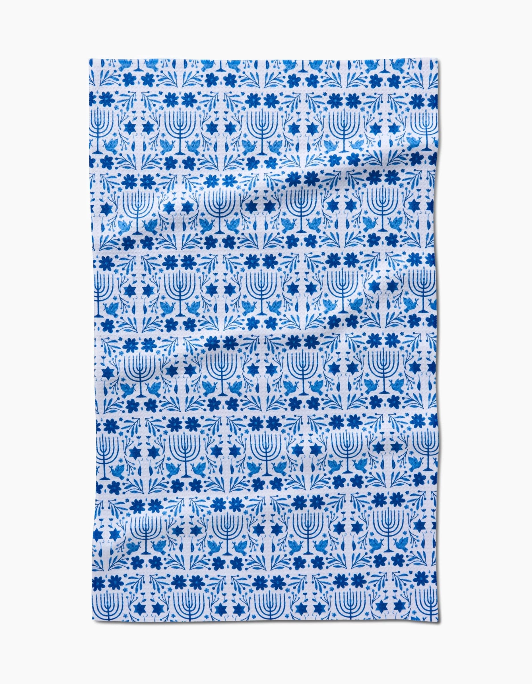 The Laura Supnik Hanukkah Kitchen Tea Towel features a blue and white menorah and floral grid pattern on Geoweave fabric, giving it a slightly wrinkled look.
