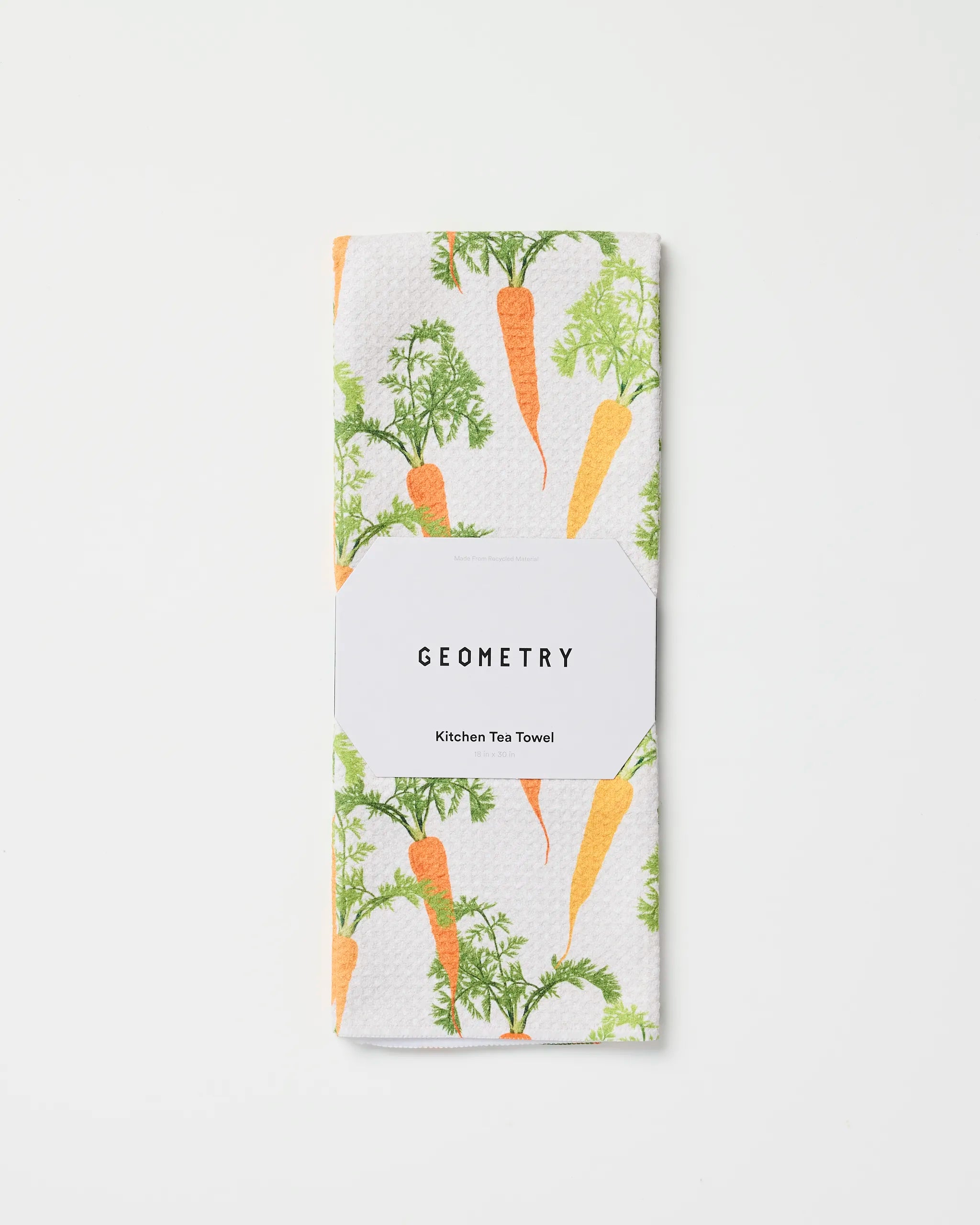 A folded white recycled kitchen towel featuring an orange carrot and green leaves pattern, labeled “Geometry Happy Carrots Kitchen Tea Towel,” displayed on a plain white background.
