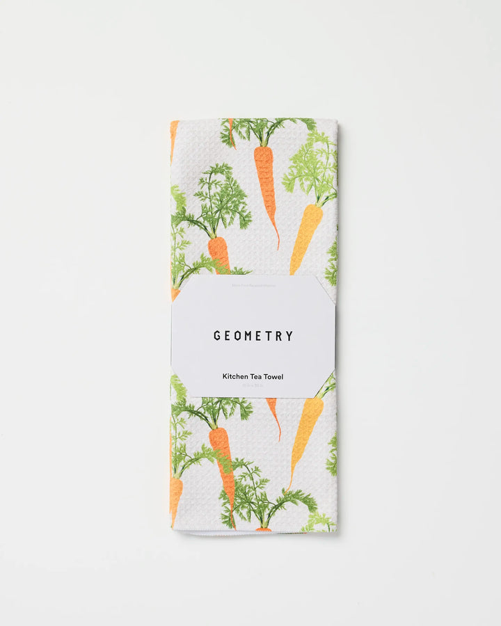 A folded white recycled kitchen towel featuring an orange carrot and green leaves pattern, labeled “Geometry Happy Carrots Kitchen Tea Towel,” displayed on a plain white background.