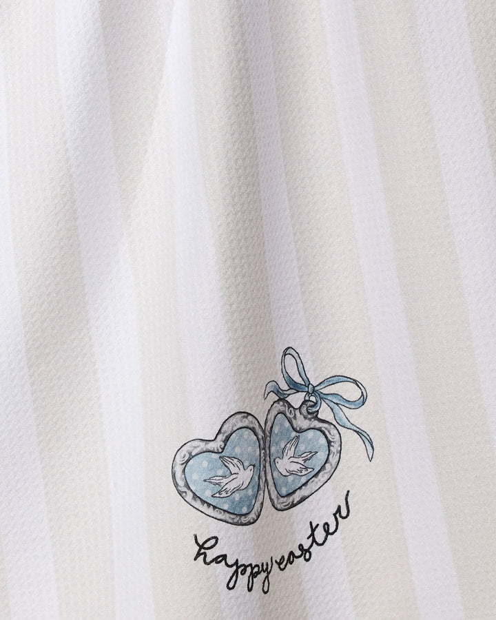 The Geometry "Happy Easter Doves" tea towel is white with subtle stripes, features two heart-shaped locket doves, a blue ribbon, "happy easter" text in handwriting, and is made from quick-drying, recycled materials.